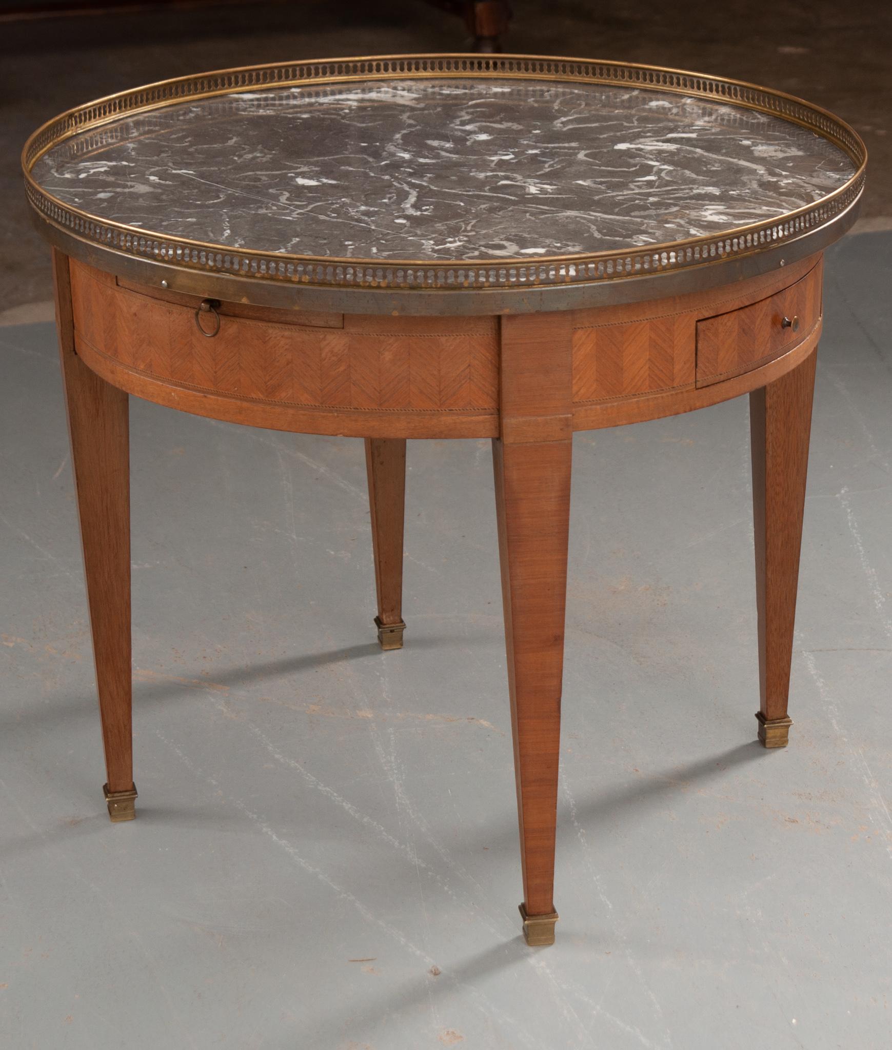 A nice example of a Louis XVI style marble-top guéridon coffee table, with brass gallery. The top is gray Saint-Anne marble with reticulated brass gallery resting over an apron of herringbone inlay wood with two drawers and two leather-topped