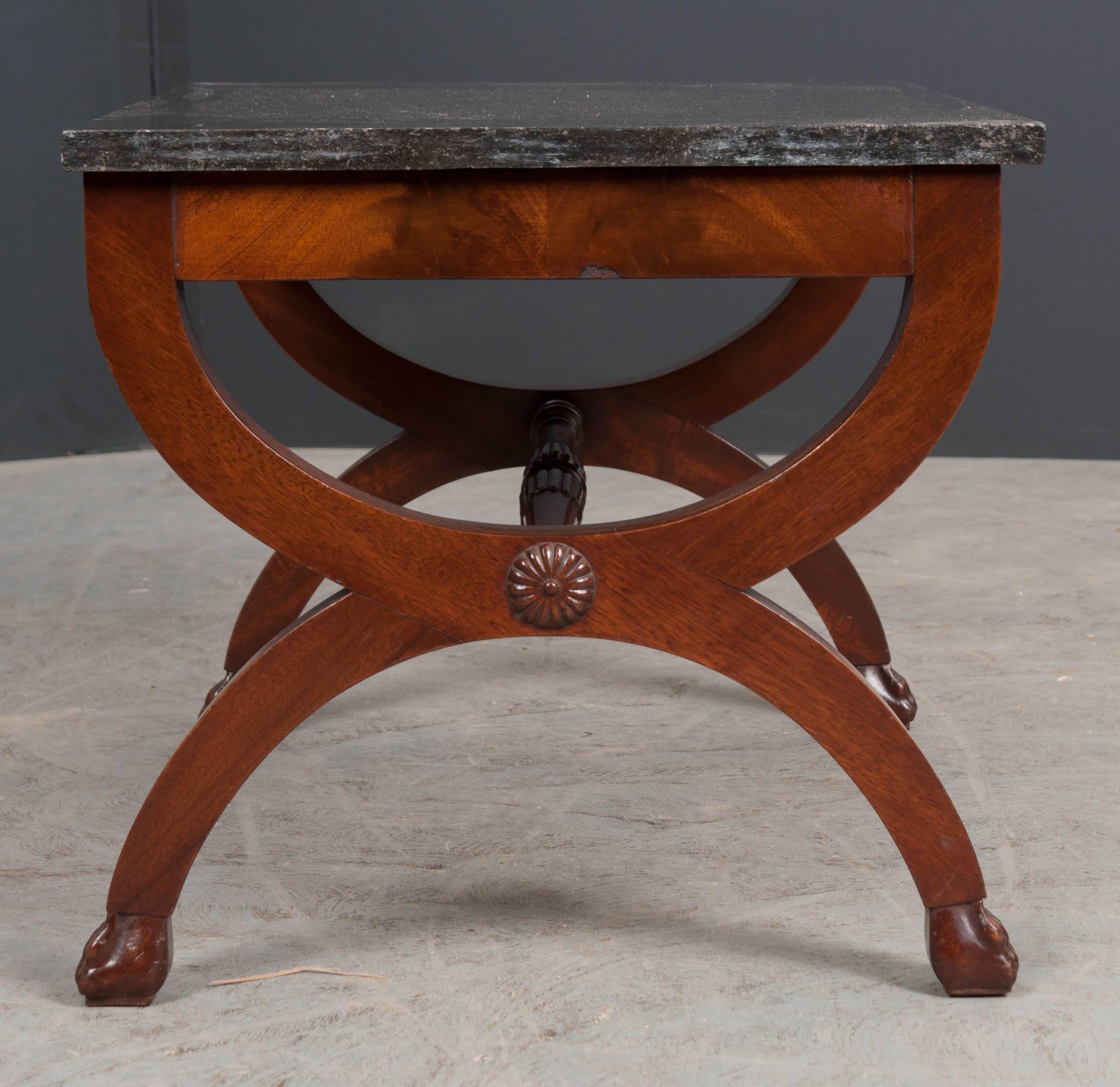 A refined coffee table, made in the French Restauration style at the end of the 19th century. The table is topped in a beautiful piece of black fossil marble. The curule-form base is braced by a turned mahogany stretcher that has been styled with