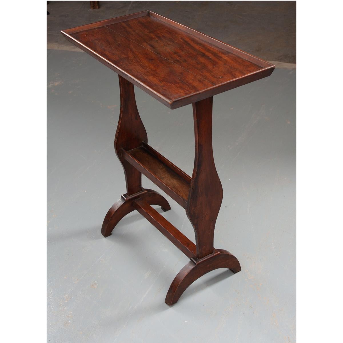 A rich, mahogany accent table from France. The rectangular table top has a beveled frame extending above the top’s surface, giving the top a tray-like appeal. This piece has shaped sides with a narrow, lower shelf, also with trim extending above the