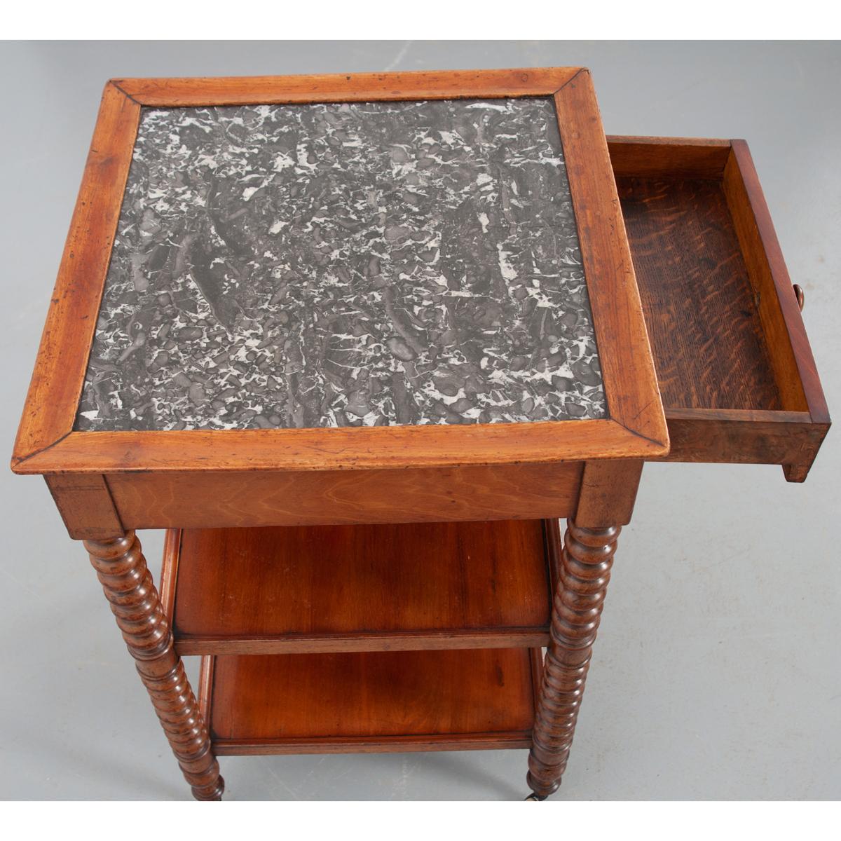 A fantastic three-tiered mahogany side table with marble top, made in France. The black and white marble-top is framed in molded trim. The apron houses a single drawer with a turned knob. Two shelves found below are also framed in molded trim and