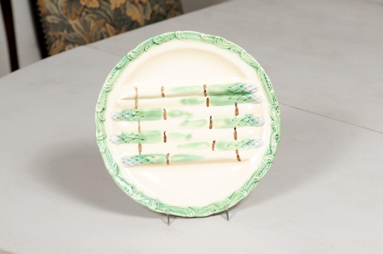 A French majolica asparagus plate from the 19th century, with green, cream, purple and brown accents. Created in France during the 19th century, this majolica plate features seven asparagus with green bodies and purple heads, resting on a cream