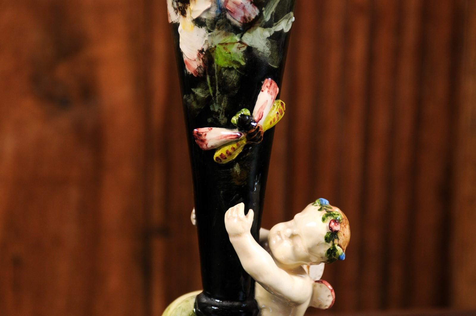 A French 19th century majolica flower vase from Montigny-sur-Loing, with cherub and dragonfly. Created in the Parisian region during the 19th century, this majolica vase features a narrow tapering body adorned with painted flowers. It is the raised