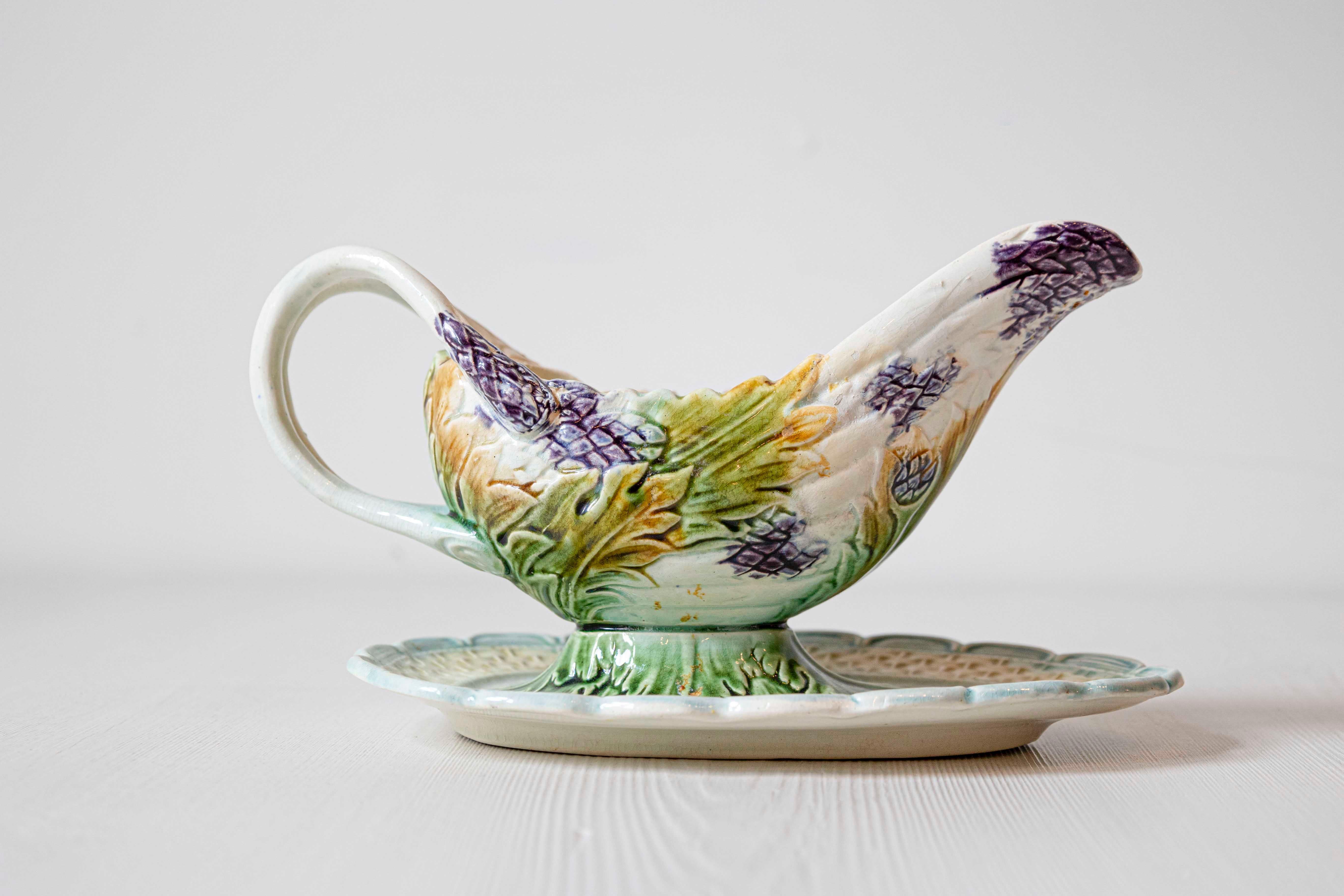 A French majolica gravy boat from the 19th century, with asparagus heads and green foliage. Created in France during the 19th century, this majolica gravy boat is adorned with a delicate décor made of purple asparagus heads and green leaves resting