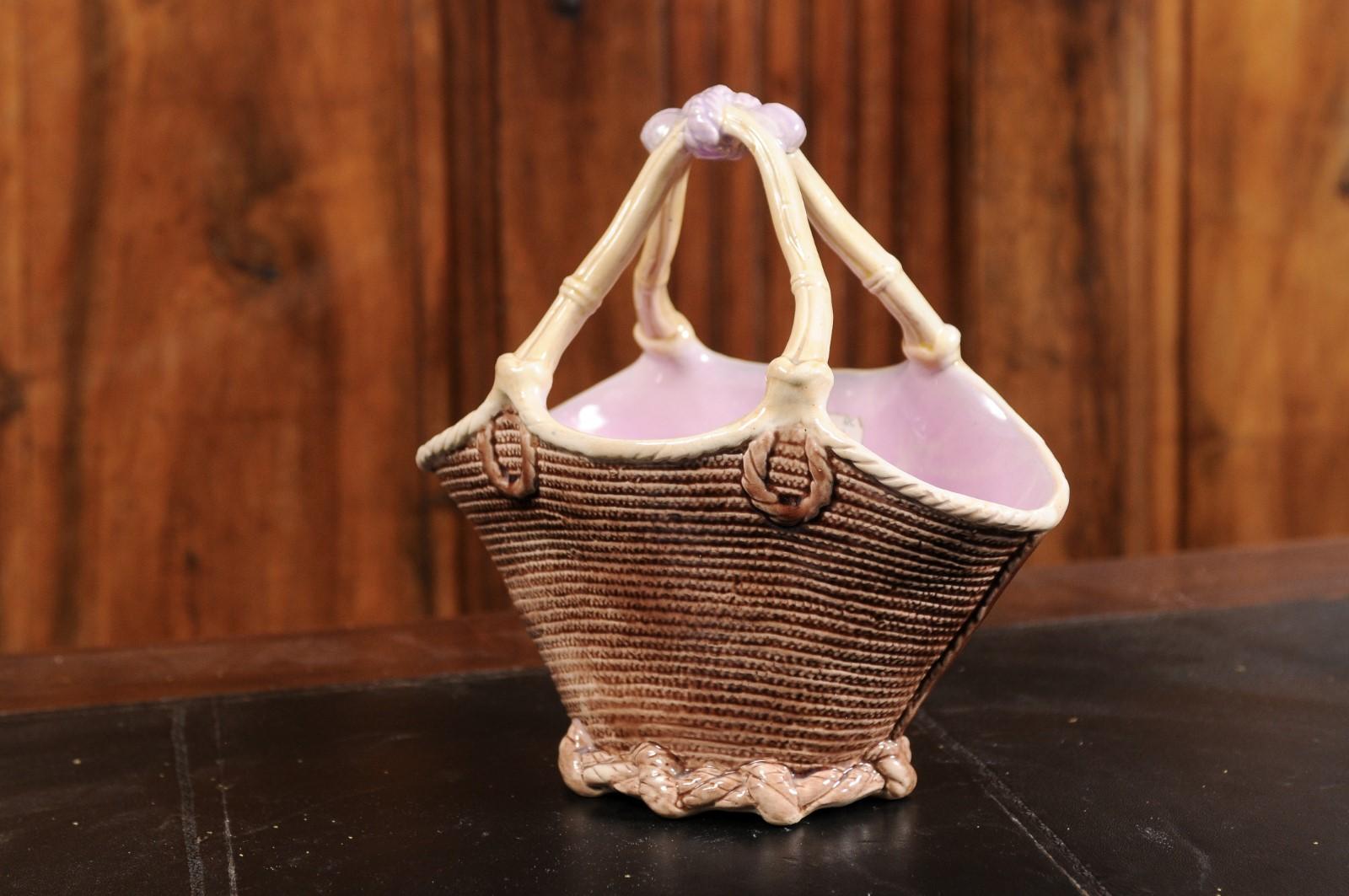 A French majolica porcelain basket from the 19th century, with wicker theme and pink glaze. Created in France during the 19th century, this majolica porcelain basket features a wicker inspired body with bamboo style handles, tied together with a