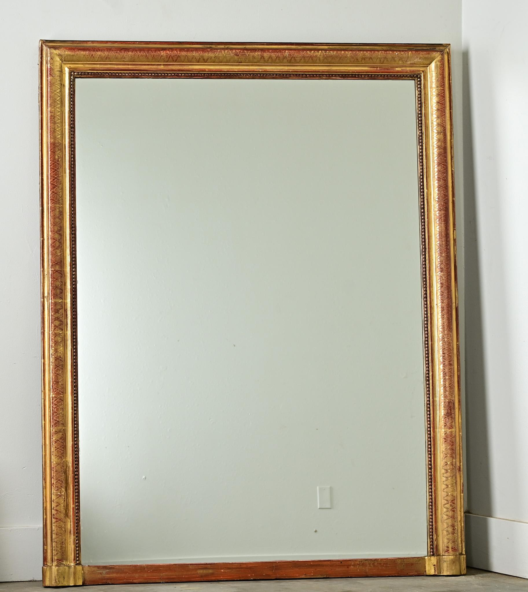 See the detailed images to appreciate how fine and subtle the texture is on this French mantel mirror. A compact trellis pattern laid out on the frame is given a festive harlequin effect by the vivacious red bole coming through the giltwork. Etched
