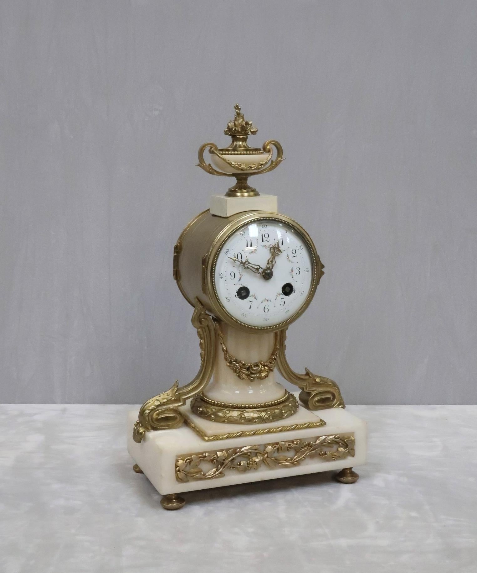 A very good quality French white marble mantel clock with fluted central column, bronze gilt inset entwining vine leaf decoration, floral swag and decorative mouldings finished with a floral urn to the top. The clock has a delicately hand painted