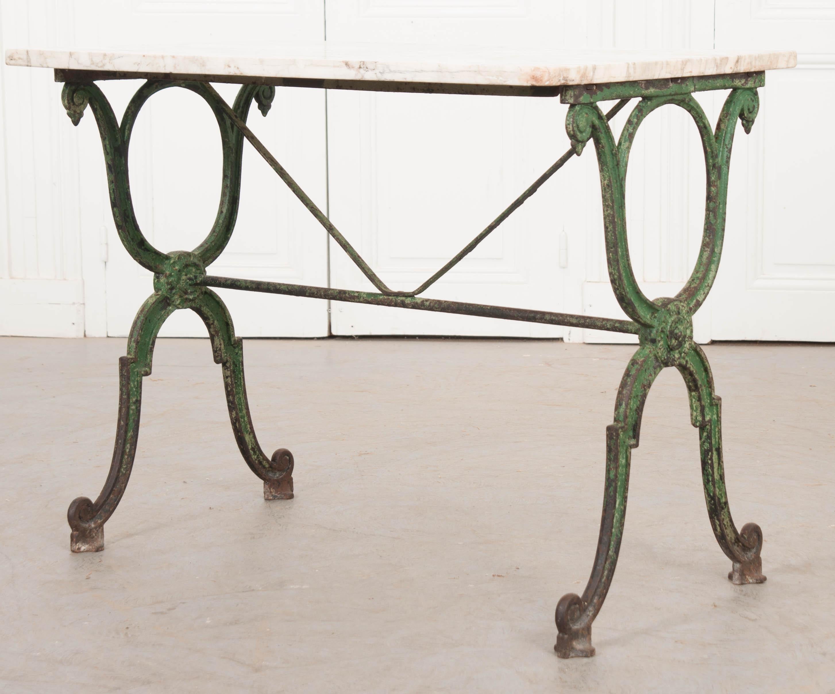 A delightful French marble-top garden table, circa 1890s, having an iron base that retains its original green paint! The white marble top has beautiful inclusions throughout. The classically styled iron base has X-form supports linked by an iron