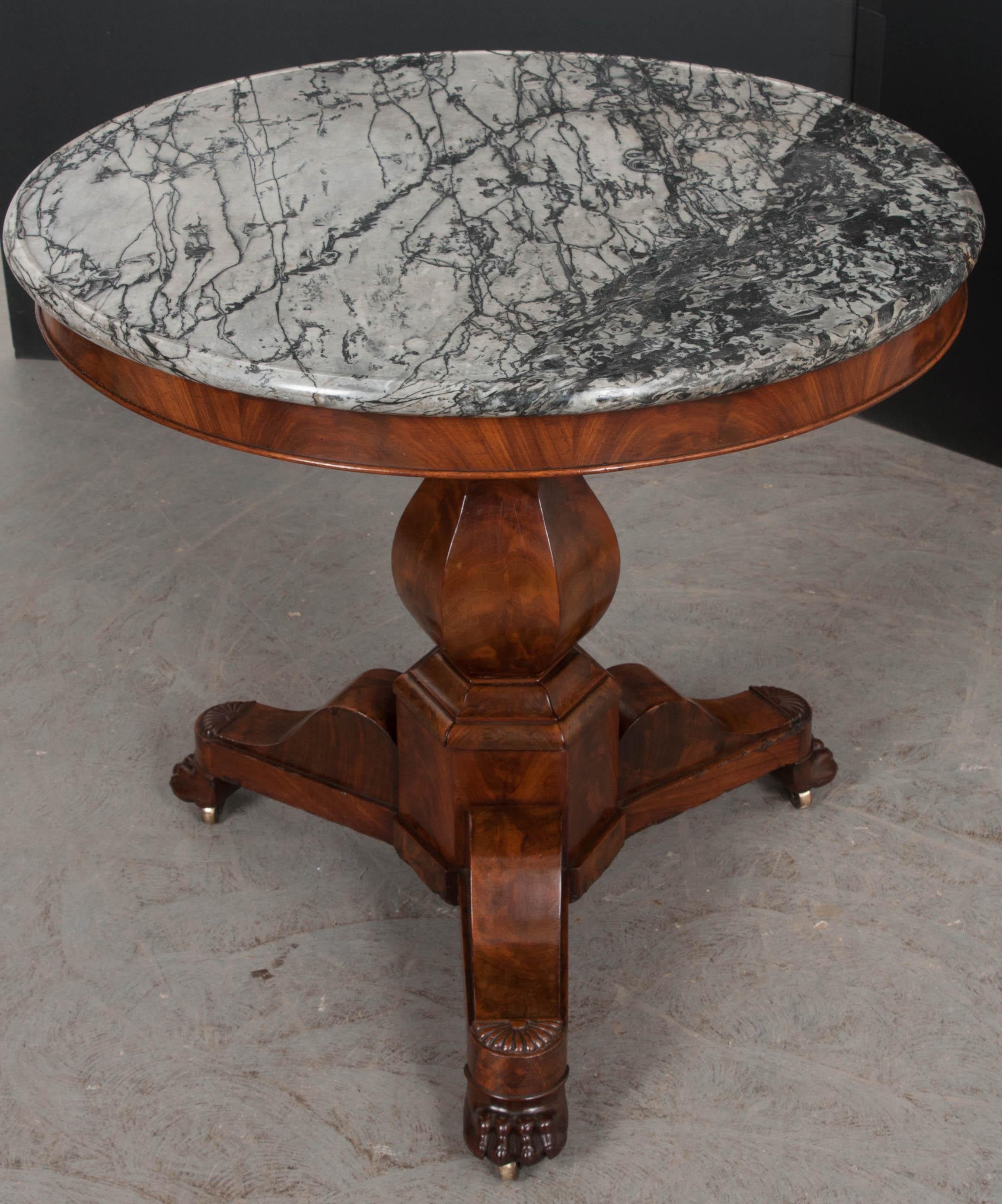 French Restauration mahogany center table, circa 1815-1830, with original dished grey-and-white marble top and beautifully veneered apron, above a hexagonal vasiform standard, and resting on a hexagonal plinth and tripodal base with well-carved claw