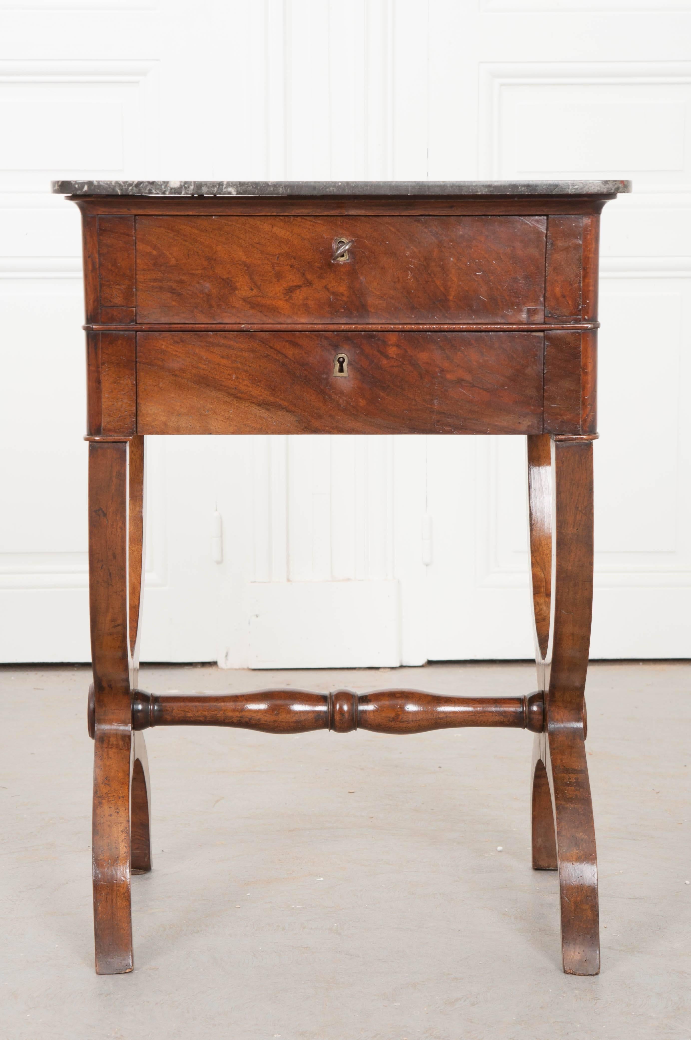 A delightful marble top table, with beautiful walnut veneer and interesting design from 19th century, France. The table has two stacked drawers, each with working locks, facilitating securable storage. The table is lifted by amazing Curule legs that