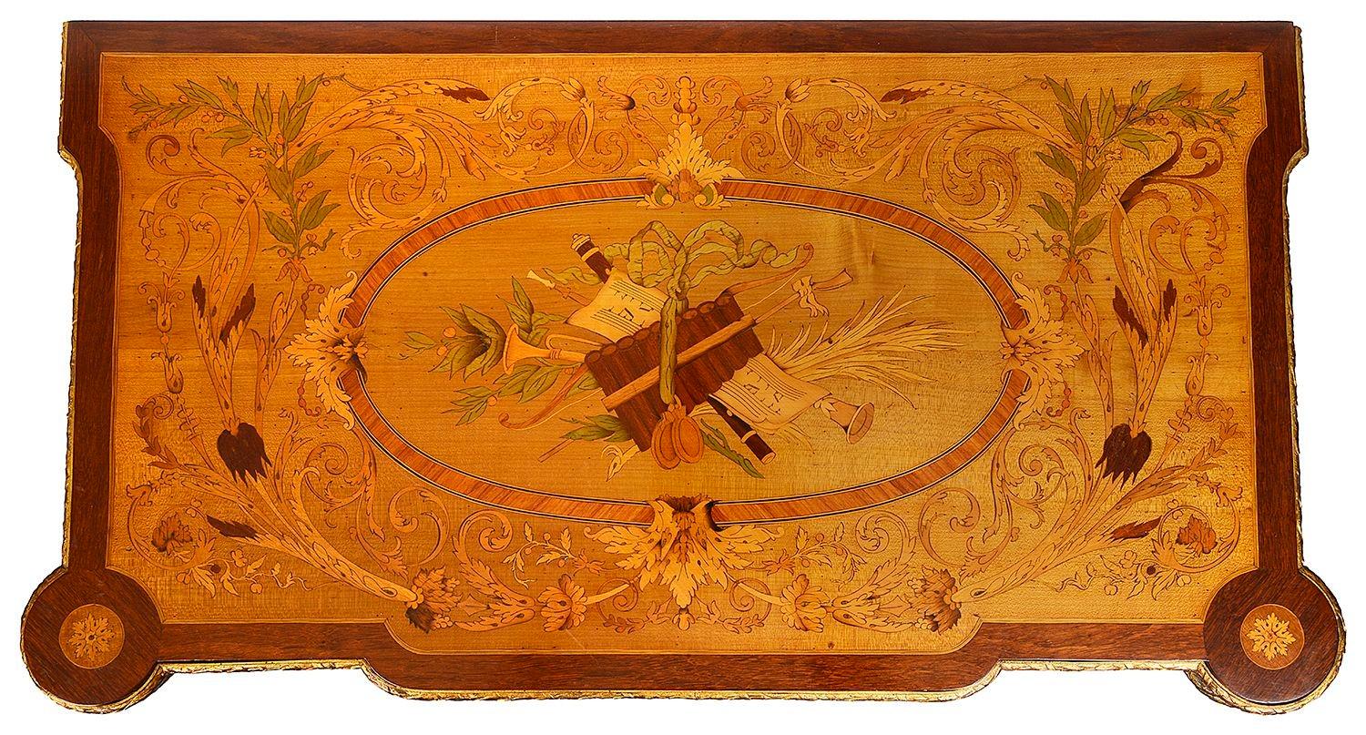 A very good quality French 19th Century marquetry inlaid card table, having musical instruments, ribbons and scrolling foliate decoration to the top, the top hinging open to reveal a baize covered card table, gilded ormolu mouldings, raised on