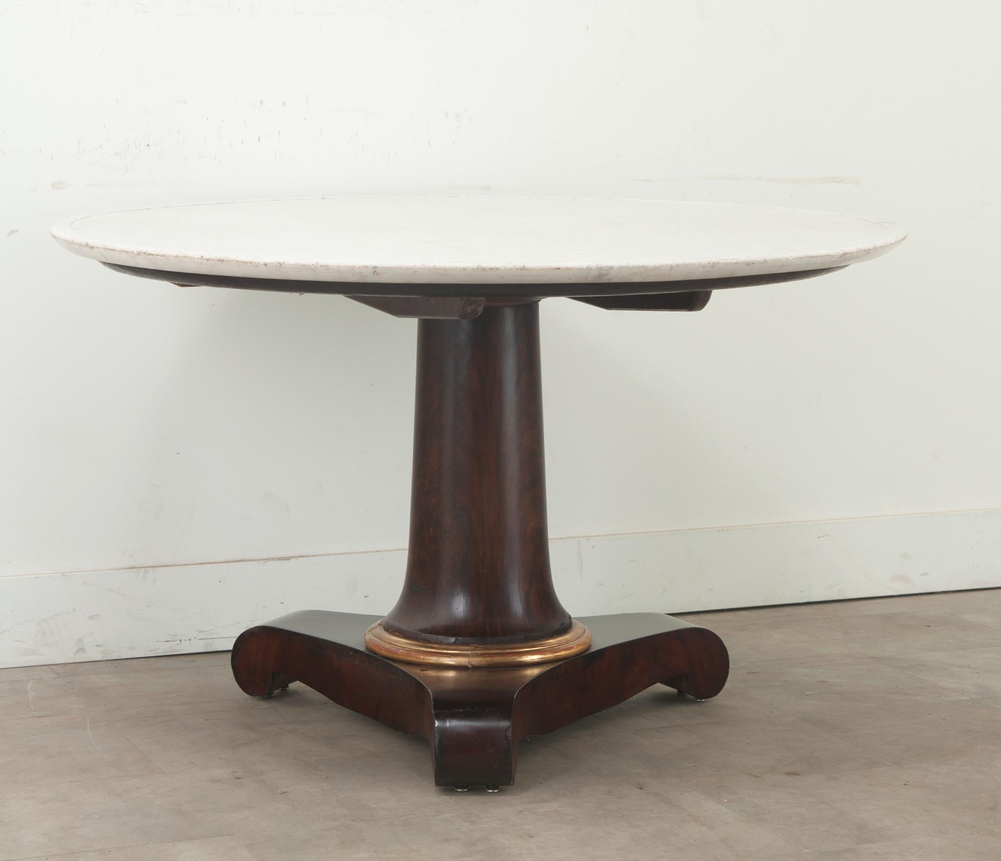 A massive French white marble top Empire Gueridon made of mahogany. The solid pedestal base has a painted and gilt collar above three splayed feet, the whole raised on working casters. The marble has been professionally repaired, be sure to view the