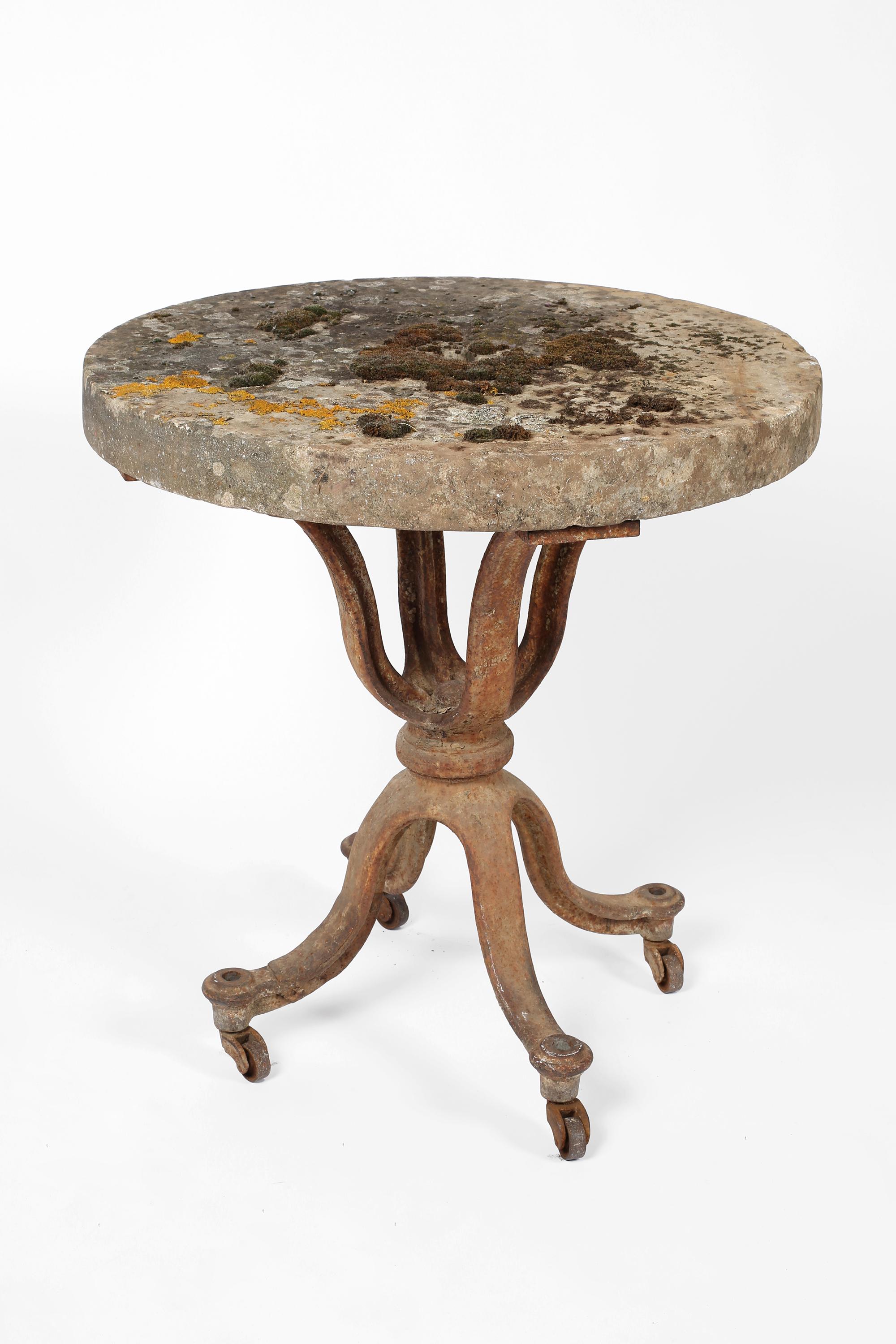 A 19th century cast iron pedestal table with earlier, circular millstone top. Heavily patinated with moss and lichen growth to the surface, with remnants of original paint and oxidisation to the base. Original castors in good working order. French,