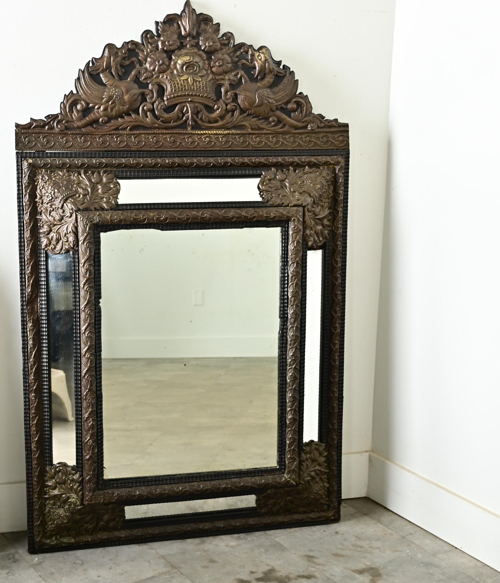 Miroir à coussin en repoussé de tradition hollandaise, datant du XIXe siècle, découpé dans une plaque de métal en haut-relief pour donner une dimension excitante, avec des serpents de mer mythiques et des motifs feuillus denses recouvrant la forme