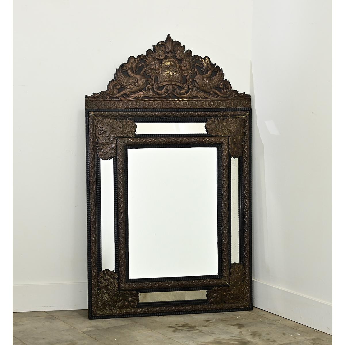 A 19th century French répoussé cushion mirror of the Dutch tradition, punched from a metal plate to high relief for exciting dimension with mythical sea serpents and dense foliate patterns covering the rectangular form. This narrative mirror in the