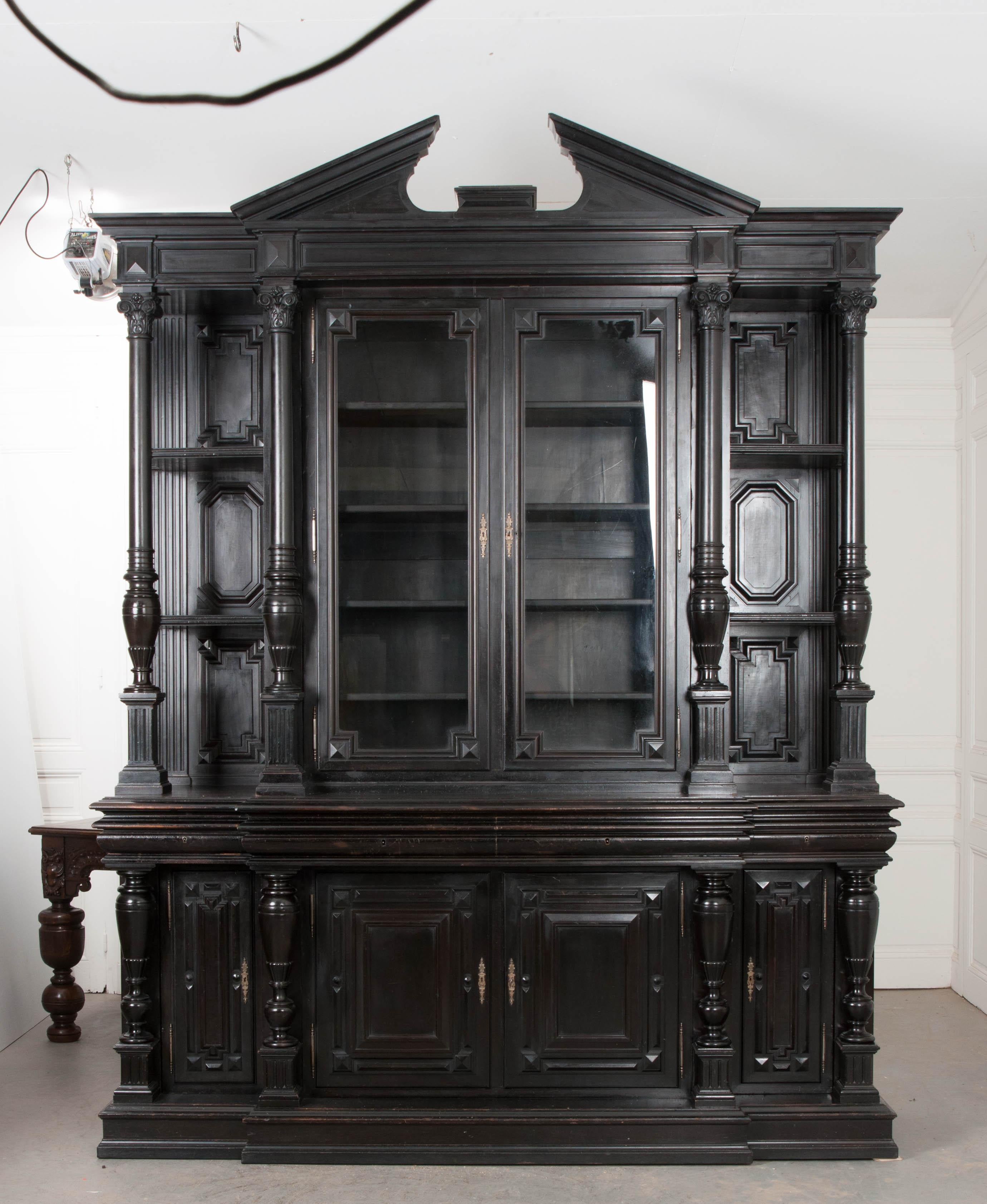 This rare, impressive, and eclectic carved Napoleon III ebonized breakfront-bibliothèque is from Paris, France, circa 1860s. It features an upper case with broken pediment and panel-carved and stepped frieze above a pair of glazed doors, through