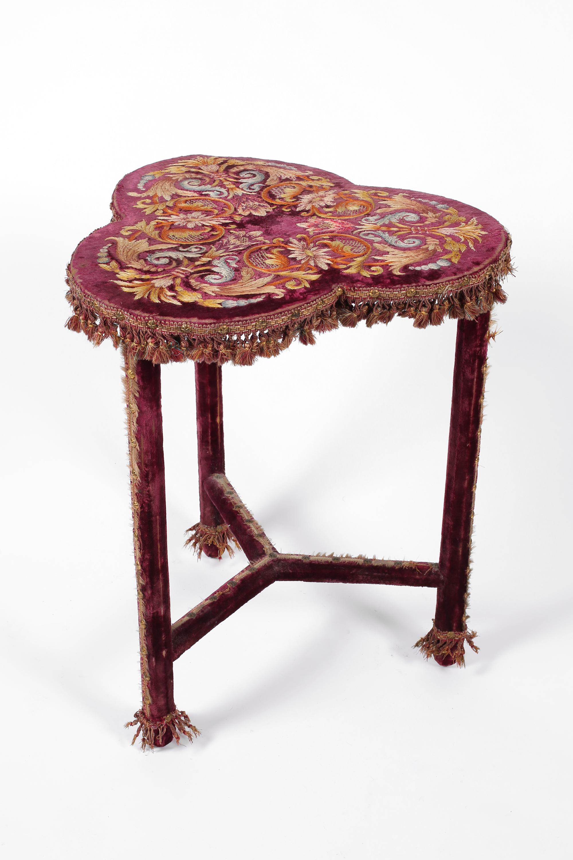 Table d'appoint Napoléon III à la broderie élaborée, tapissée d'un riche velours rouge amarante, avec des motifs floraux/foliacés complexes sur le plateau trilobé. Probablement utilisée à l'origine comme table de jeu, la surface en tissu de