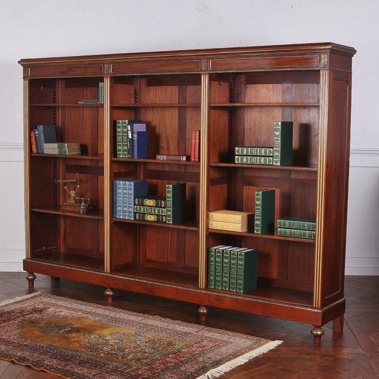 A 19th century French Napoleon III open bookcase in mahogany with brass accents. The piece features three sections separated by fluted gilt pilasters, each section with four adjustable shelves (shown with only three shelves in the photos but there