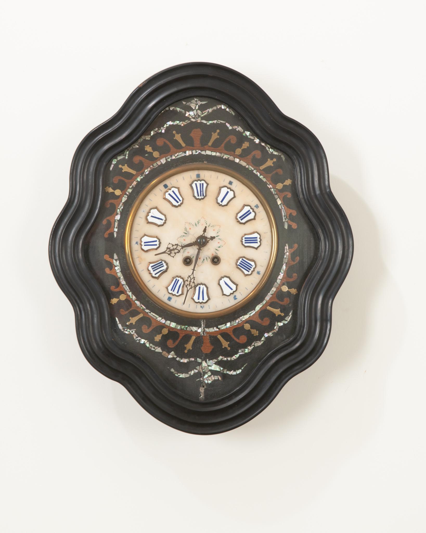 Cette horloge du 19e siècle est étonnante avec son cadre en bois peint à l'ébène en forme de losange ondulé. Des motifs floraux et feuillagés en nacre sont incrustés dans de l'acajou teinté différemment et de la nacre brillante, entourant le cadran