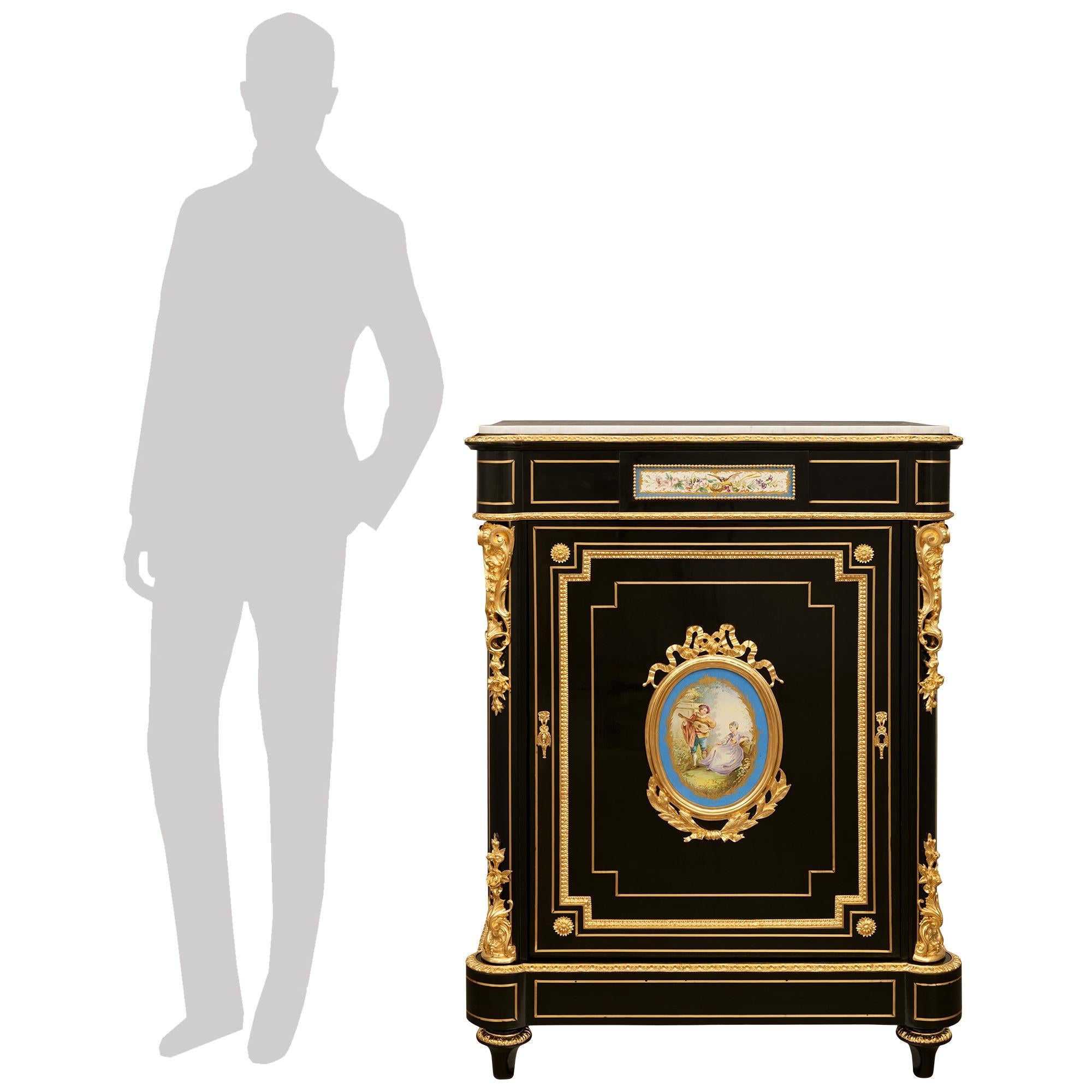 A handsome French 19th century Napoleon III Period Ebony, Sèvres Porcelain, Brass, Ormolu and Marble cabinet. The stunning single door cabinet is raised by toupie shaped Ebony feet accented with top Ormolu foliate bands. The toupie shaped supports