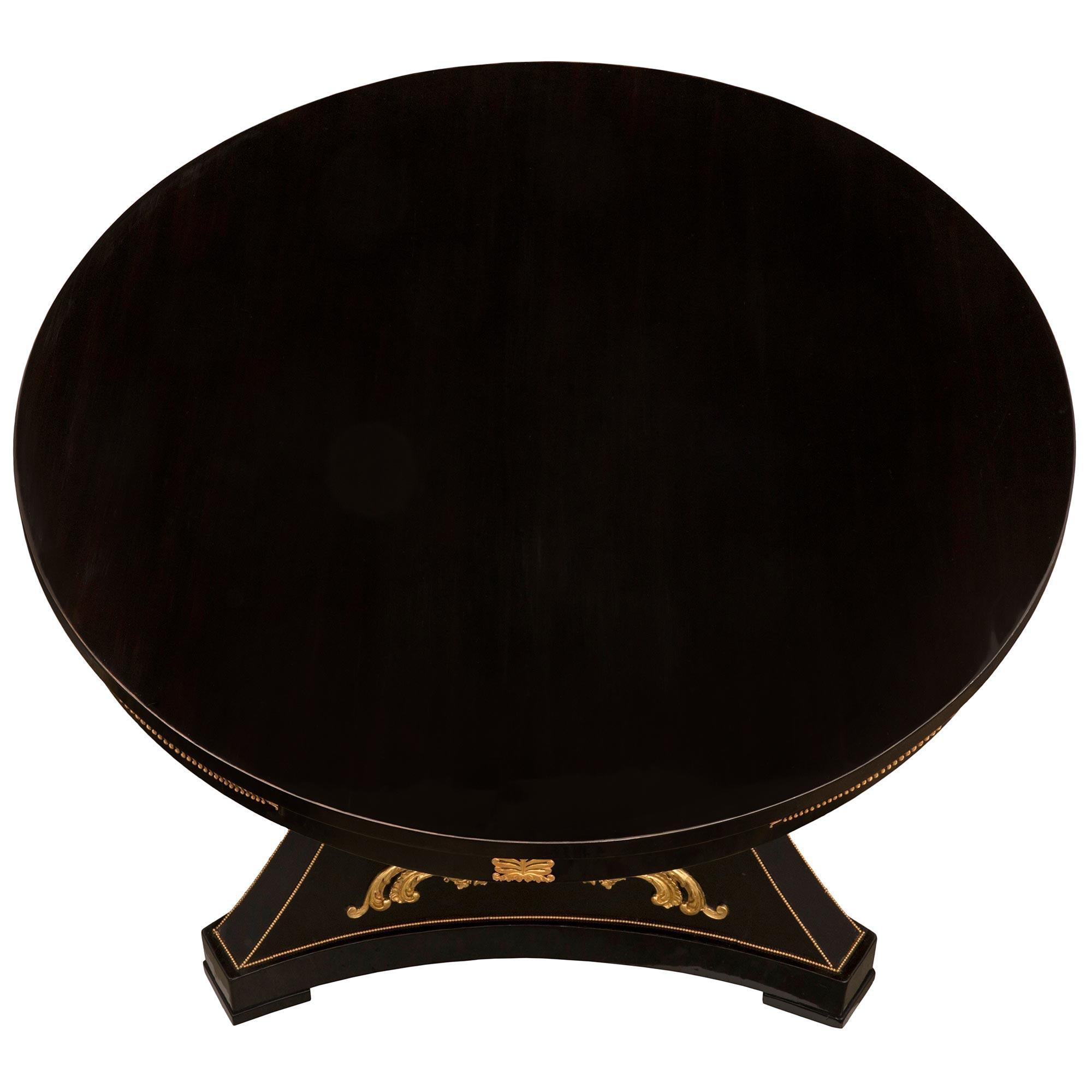 Impressionnante table centrale en ébène, bronze doré et bois doré d'époque Napoléon III. La table circulaire est surélevée par un support triangulaire élégamment incurvé avec des coins coupés et des côtés concaves, le tout au-dessus des roulettes