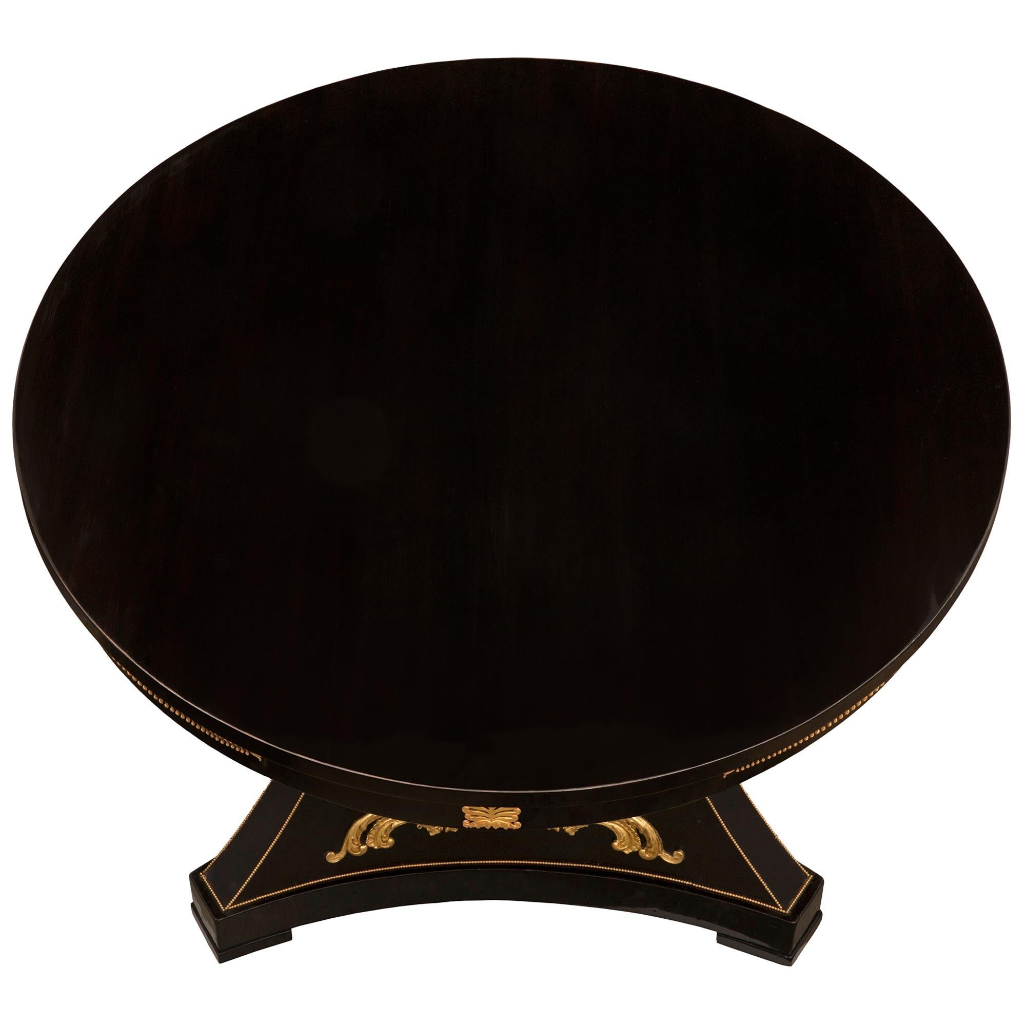 Impresionante mesa central francesa del siglo XIX, época de Napoleón III, de ébano, ormolu y madera dorada. La mesa circular se eleva sobre un soporte triangular elegantemente curvado, con esquinas recortadas y lados cóncavos, todo ello sobre las