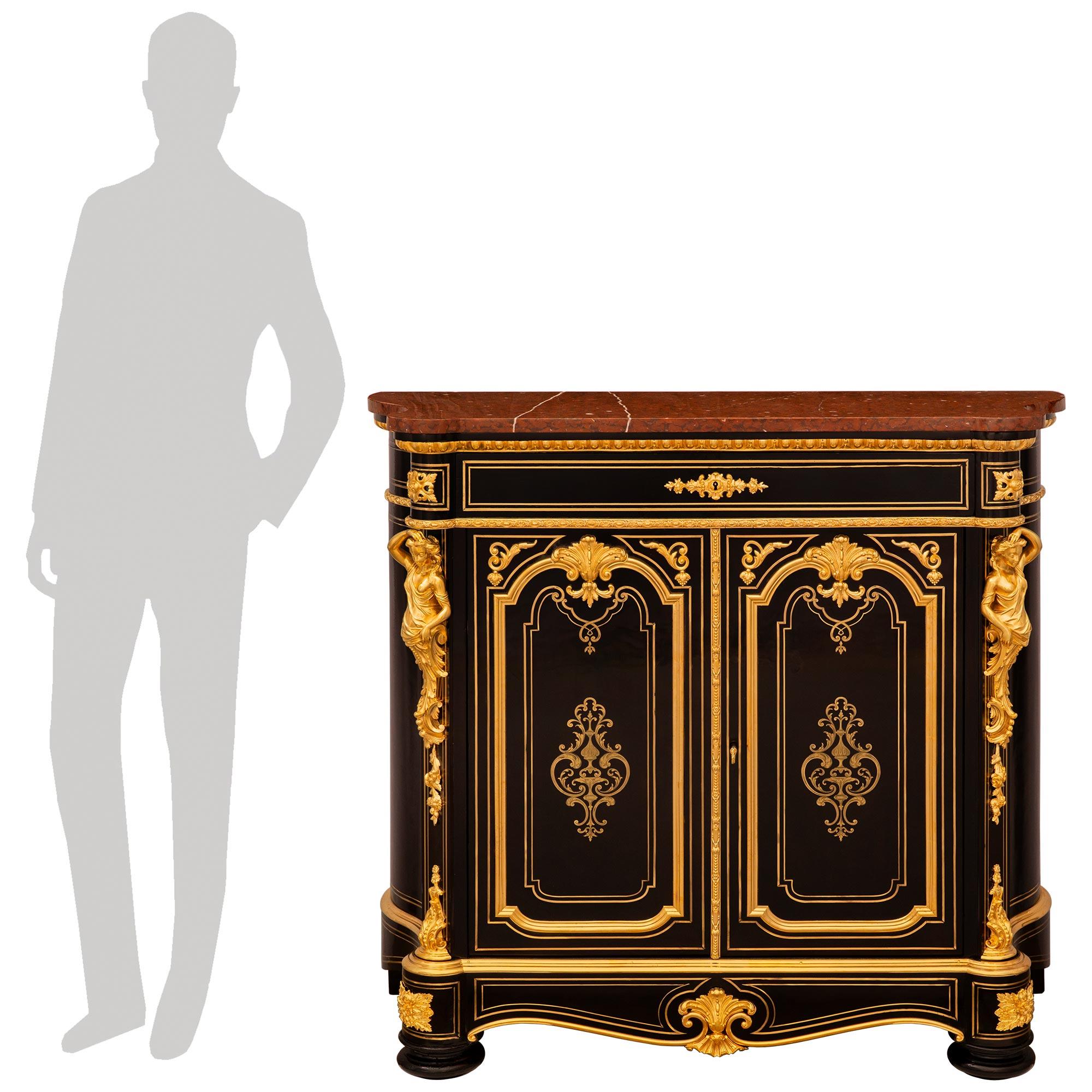 A stunning and high quality French 19th century Napoleon III Period Louis XVI st. Ebony, Ormolu, Giltwood and Rouge Griotte marble cabinet. This exquisite two door single drawer cabinet is raised on two Ebony bun feet in the front and two block feet