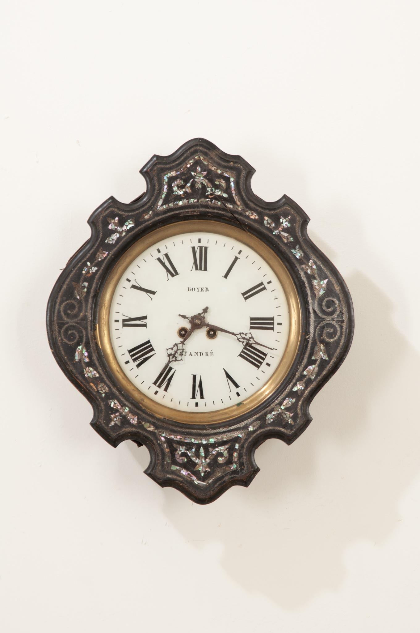 This 19th century clock is stunning with its shaped frame of ebonized wood. Mother-of-pearl floral designs are inlaid in brilliant mother-of-pearl, surrounding the porcelain clock face in symmetrical form. Behind protective glass, the white