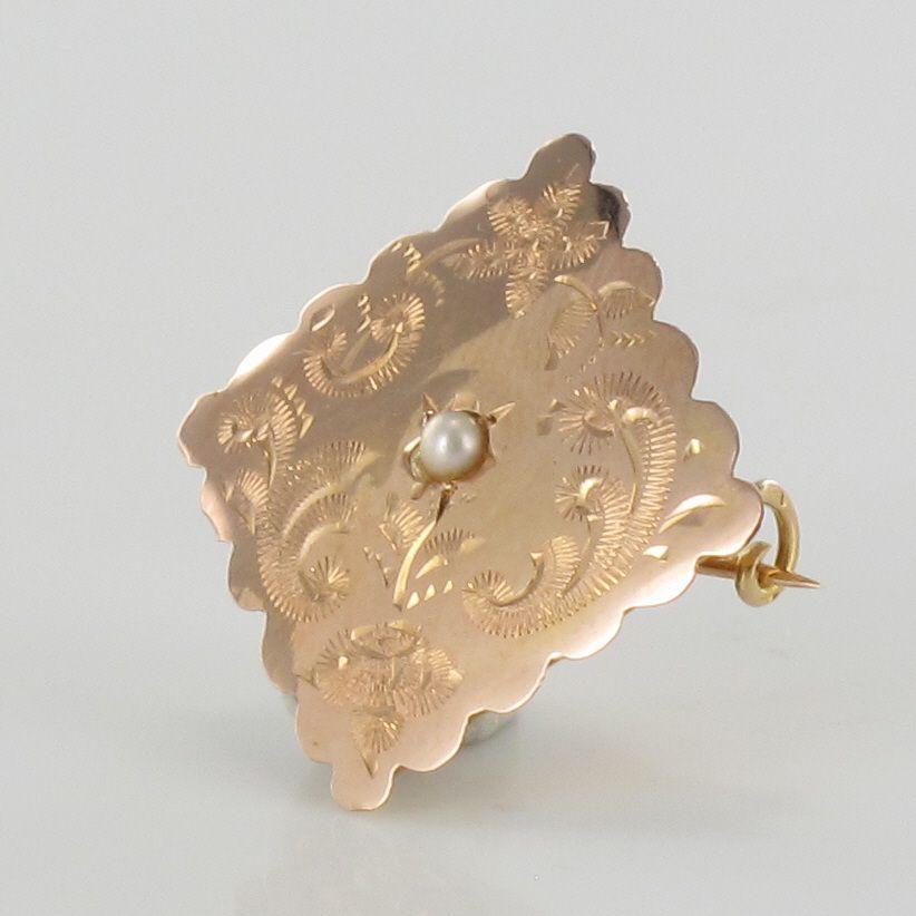 Brooch in 18 karat rose gold, eagle's head hallmark.
Lovely lozenge-shaped brooch, it is chiseled on its top with an arabesque decoration and centered with a natural half pearl. The clasp is a pin with a safety hook.
Height : 2.1 cm, width : 2.1