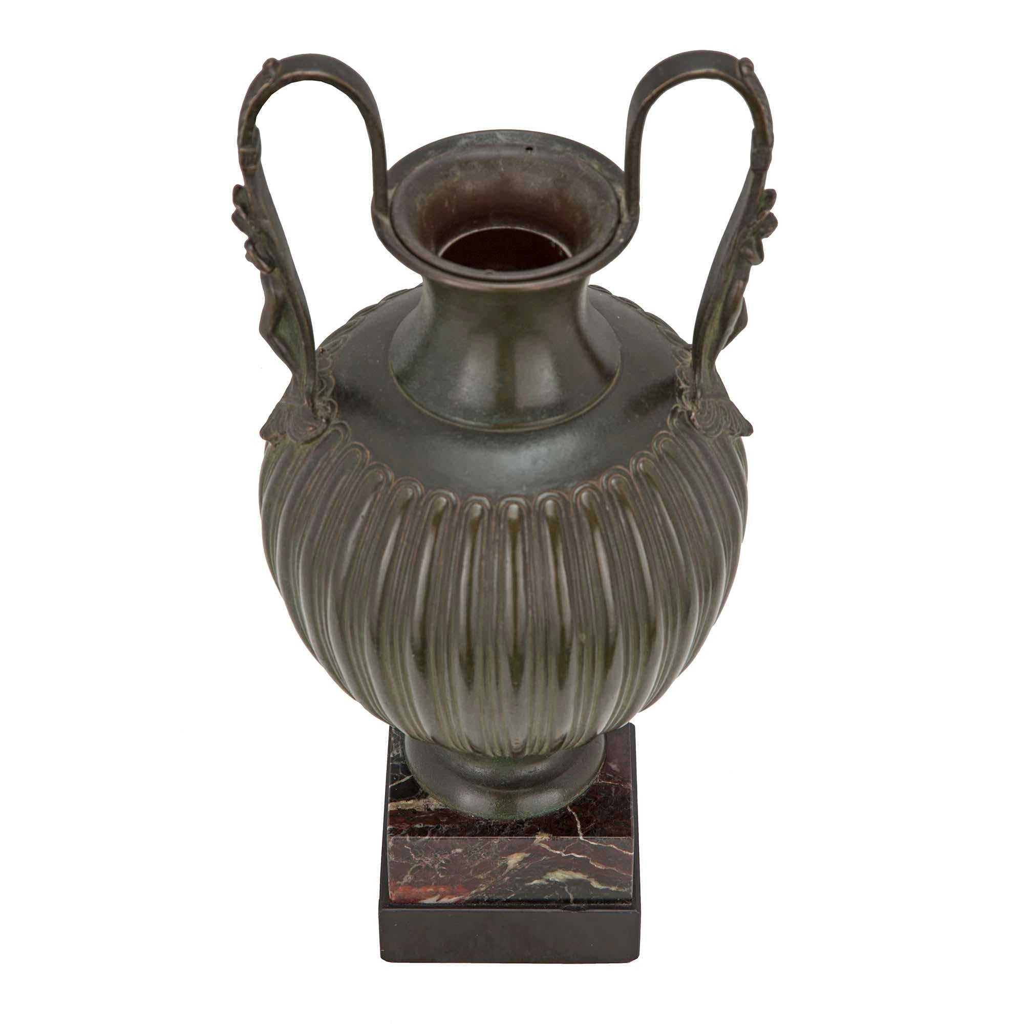 Bellissima urna neoclassica francese del XIX secolo in bronzo patinato verdastro. L'urna è sollevata su una base quadrata di marmo. La bella urna in bronzo patinato verdastro ha una forma a balaustro con nervature. Su ogni lato ci sono eleganti