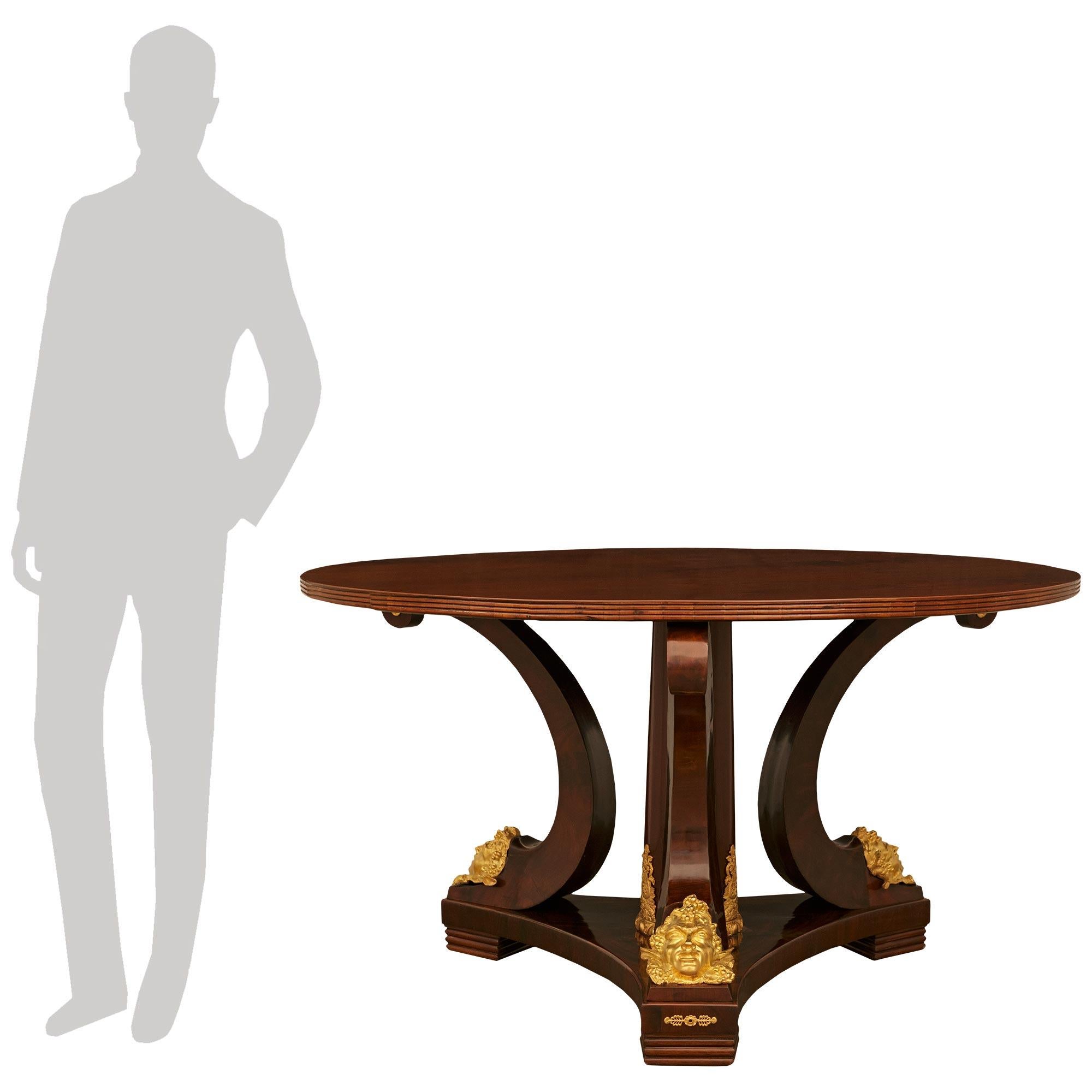 A handsome and most impressive French 19th century Neo-Classical st. Flame Mahogany and Ormolu center table. This stunning table is raised on a triangular base with concave sides and pierced Ormolu mounts on the façade of each foot. Above are three