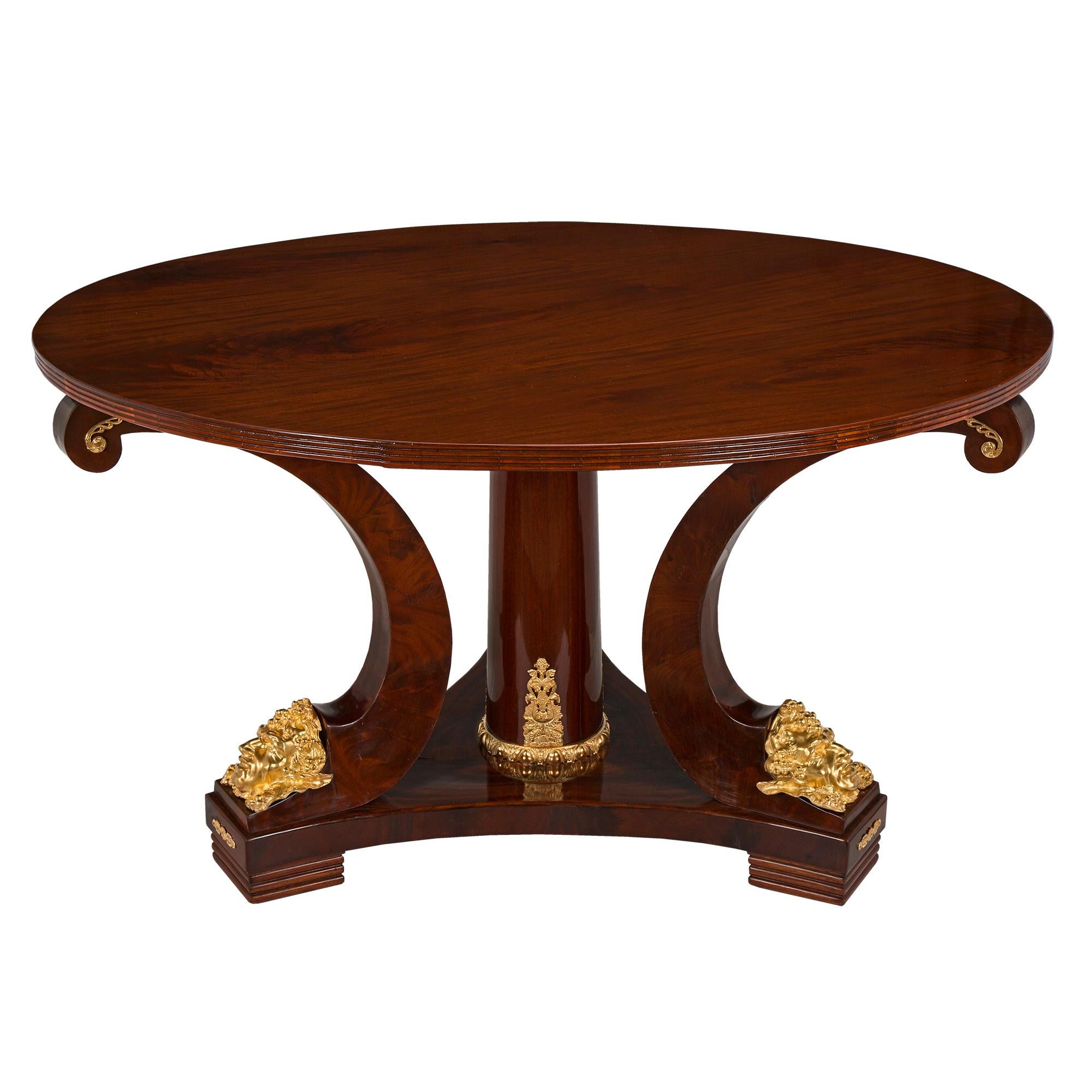 A very handsome French 19th century neo-classical st. flamed mahogany and ormolu center table. The table is raised on a triangular base with concave sides and pierced ormolu mounts on the façade of each foot. Above are three elegant C scrolled