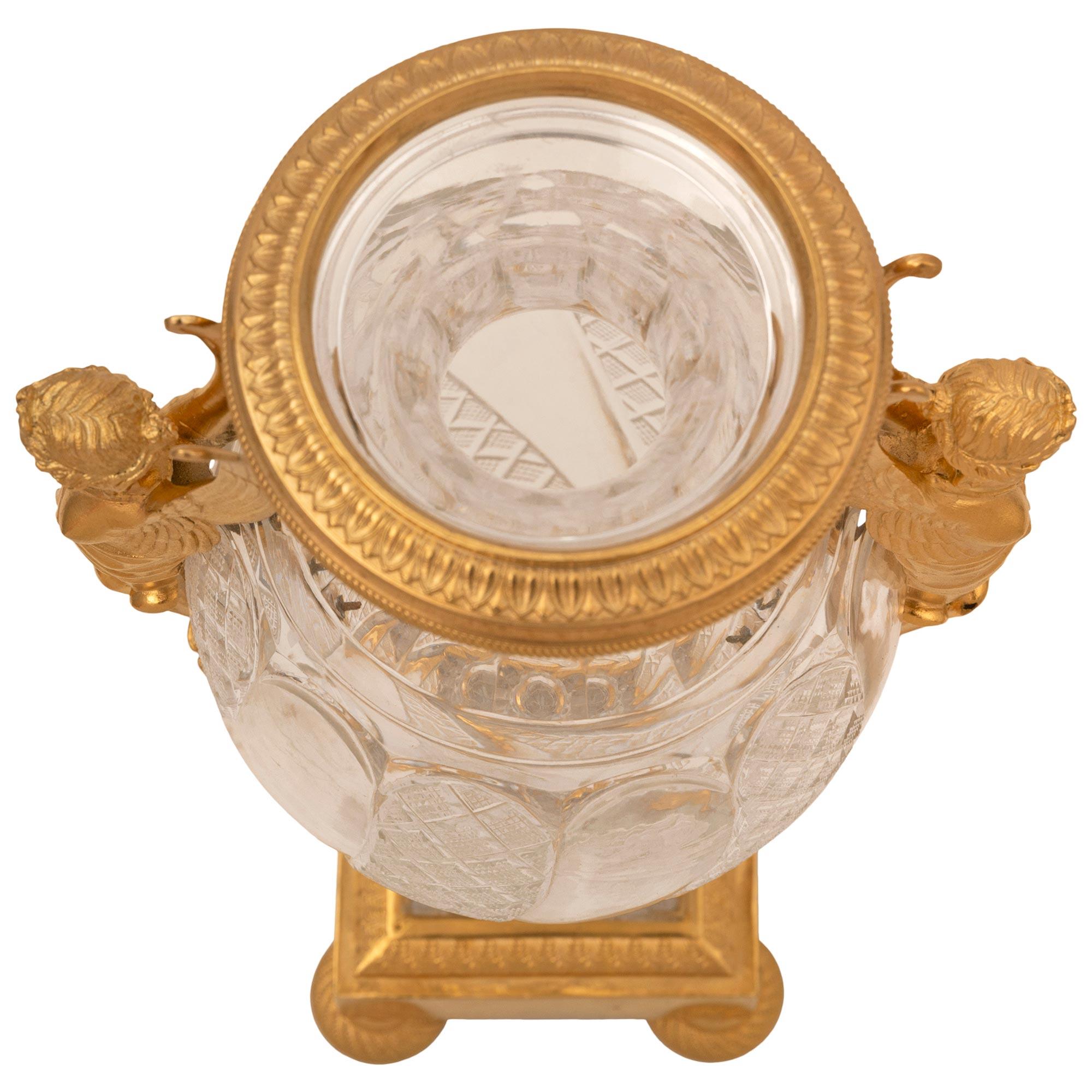 Magnifique urne néo-classique du XIXe siècle en bronze doré et cristal de Baccarat. L'urne est surmontée d'une base carrée avec d'élégants pieds en chignon, de magnifiques motifs en spirale gravés et perlés, et d'une bande de palmettes marbrées.