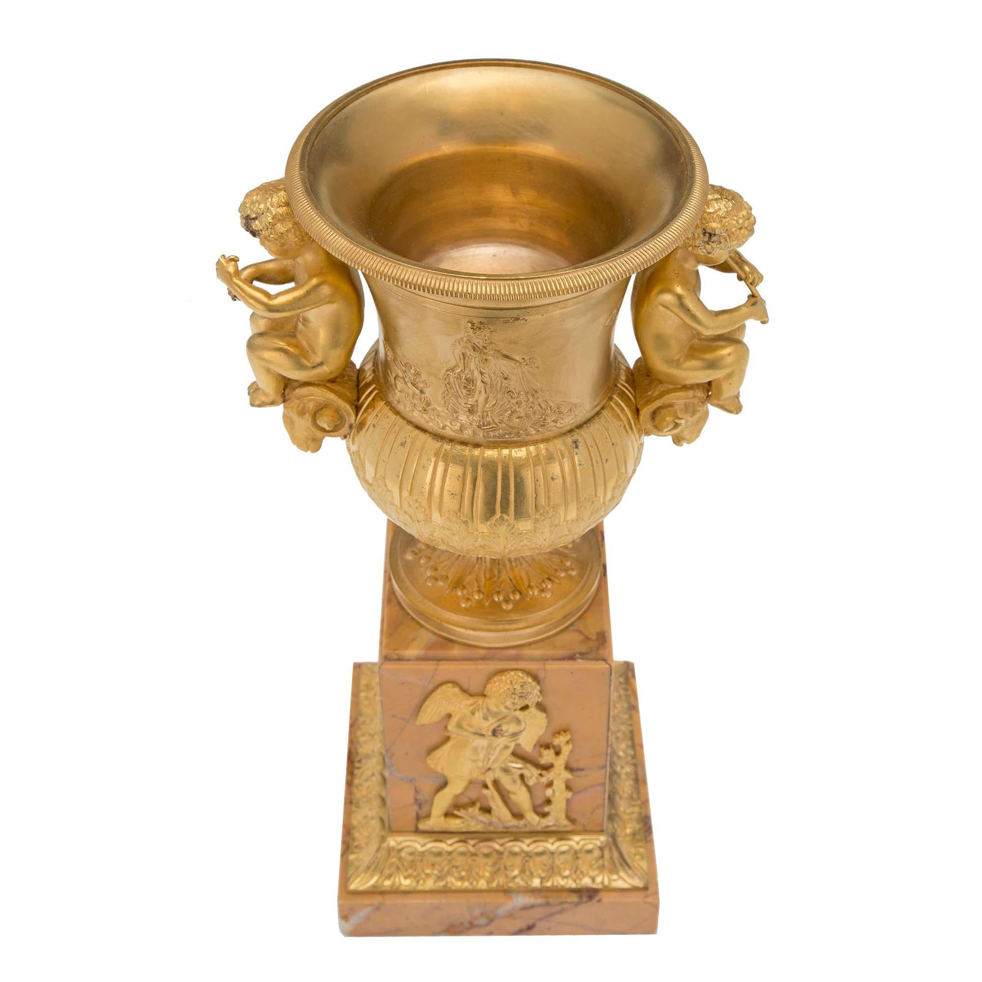 Paire d'urnes néo-classiques françaises du XIXe siècle en bronze doré et marbre de Sienne. Chaque urne repose sur une base carrée avec une bordure feuillagée en bronze doré. La colonne carrée est surmontée de montures en bronze doré finement
