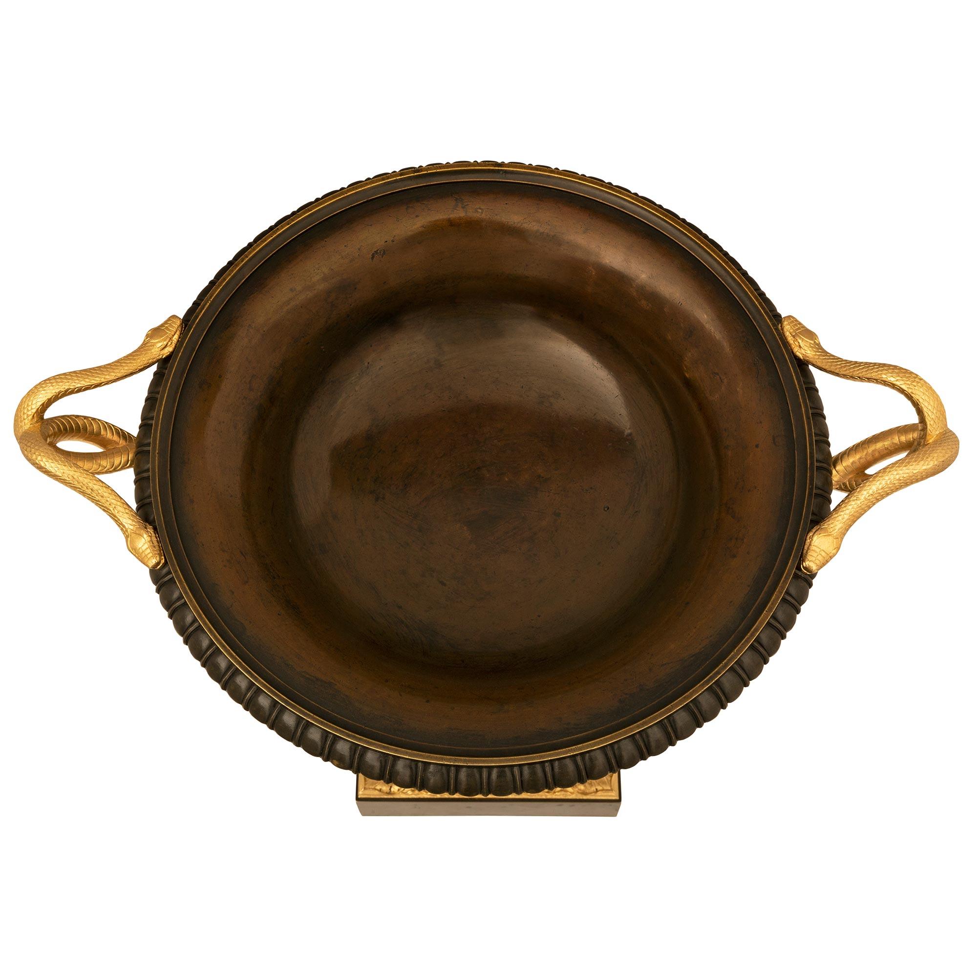 Remarquable tazza en bronze patiné et bronze doré de très haute qualité, de style néoclassique français du XIXe siècle. La tazza repose sur une base carrée ornée d'une belle bande de bronze doré à feuillage tacheté et de belles couronnes de laurier