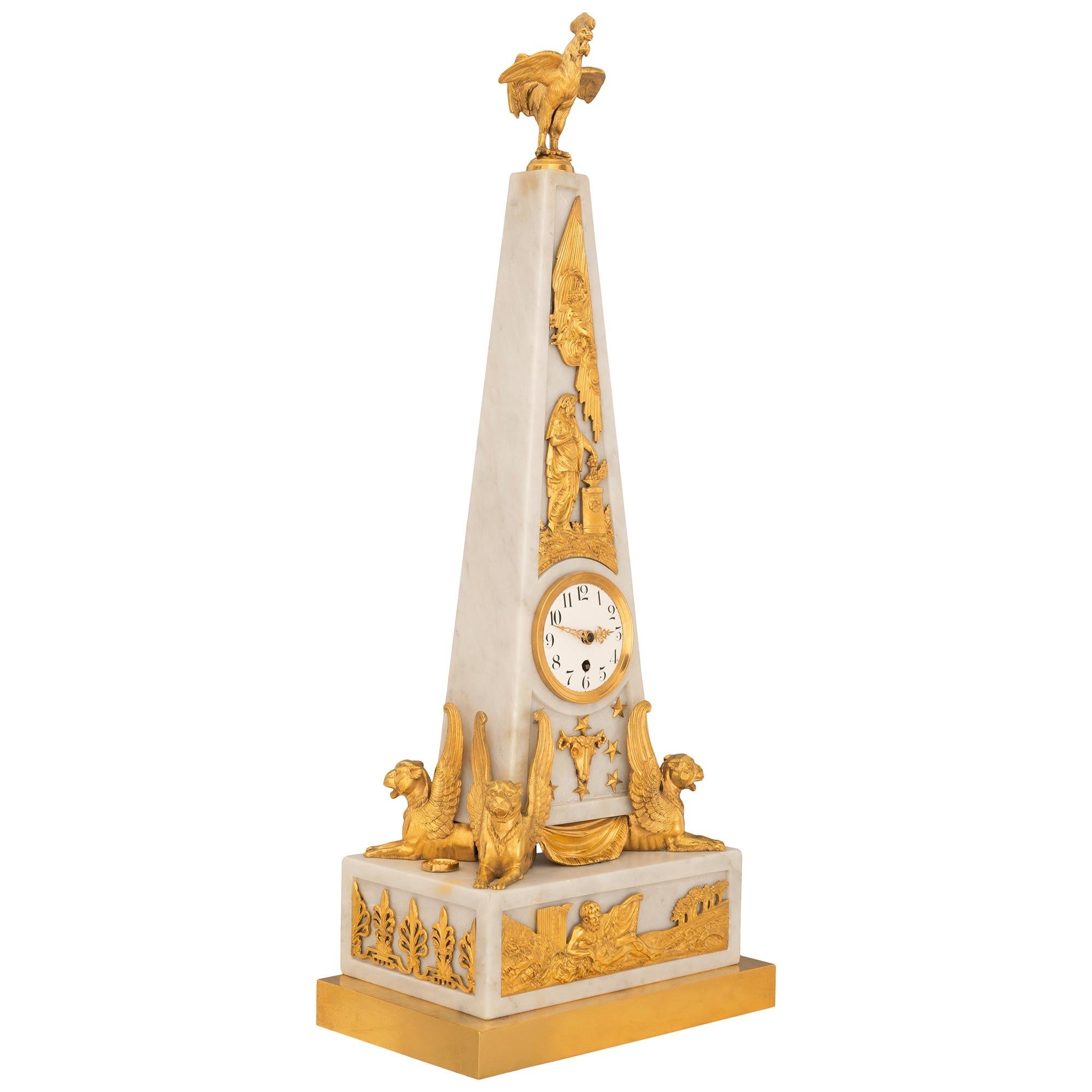 A striking and unique French early 19th century Neo-Classical st. white Carrara marble and ormolu obelisk shaped clock. The clock is raised by a rectangular white Carrara marble base with a thick bottom ormolu band and superb richly chased fitted