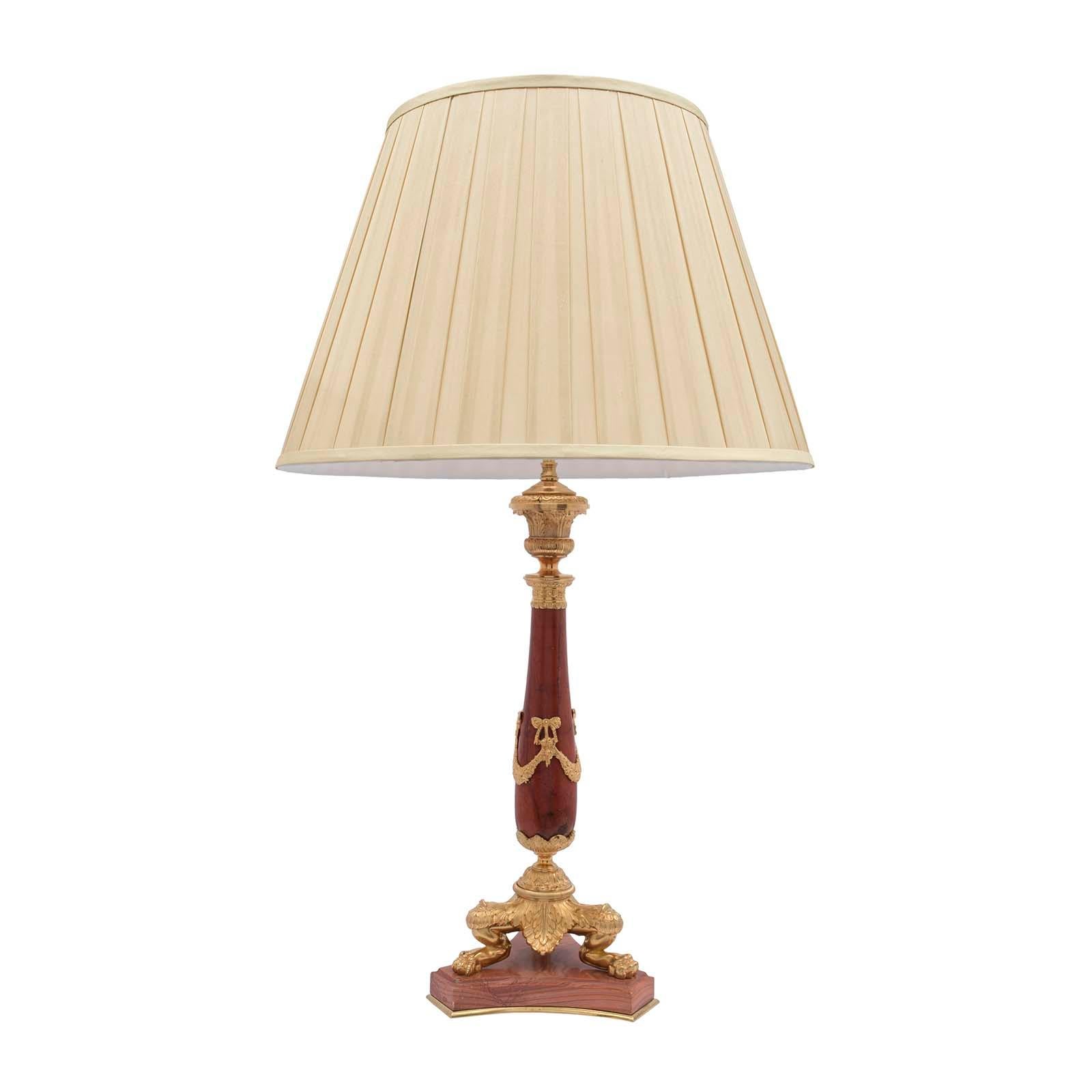 A handsome French 19th century neo-classical st. red marble and ormolu lamp. The lamp is raised by a triangular marble base with concave sides, a mottled border and a bottom ormolu filet. At the base are three richly chased ormolu paw feet amidst