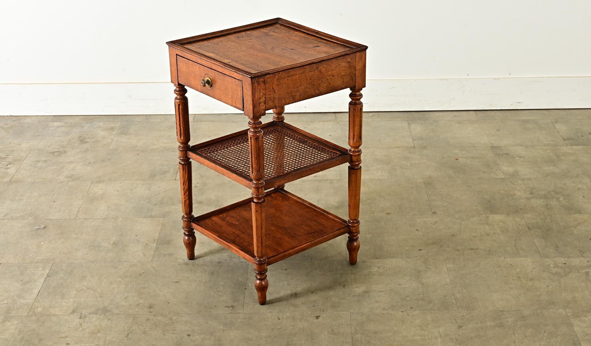 A small French oak and cane etagere, circa 1880, that would make a smart bedside table or end table where space is limited. The top surface, inset by a low frame, showcases the characteristic grain pattern of antique oak–with all its patina–and