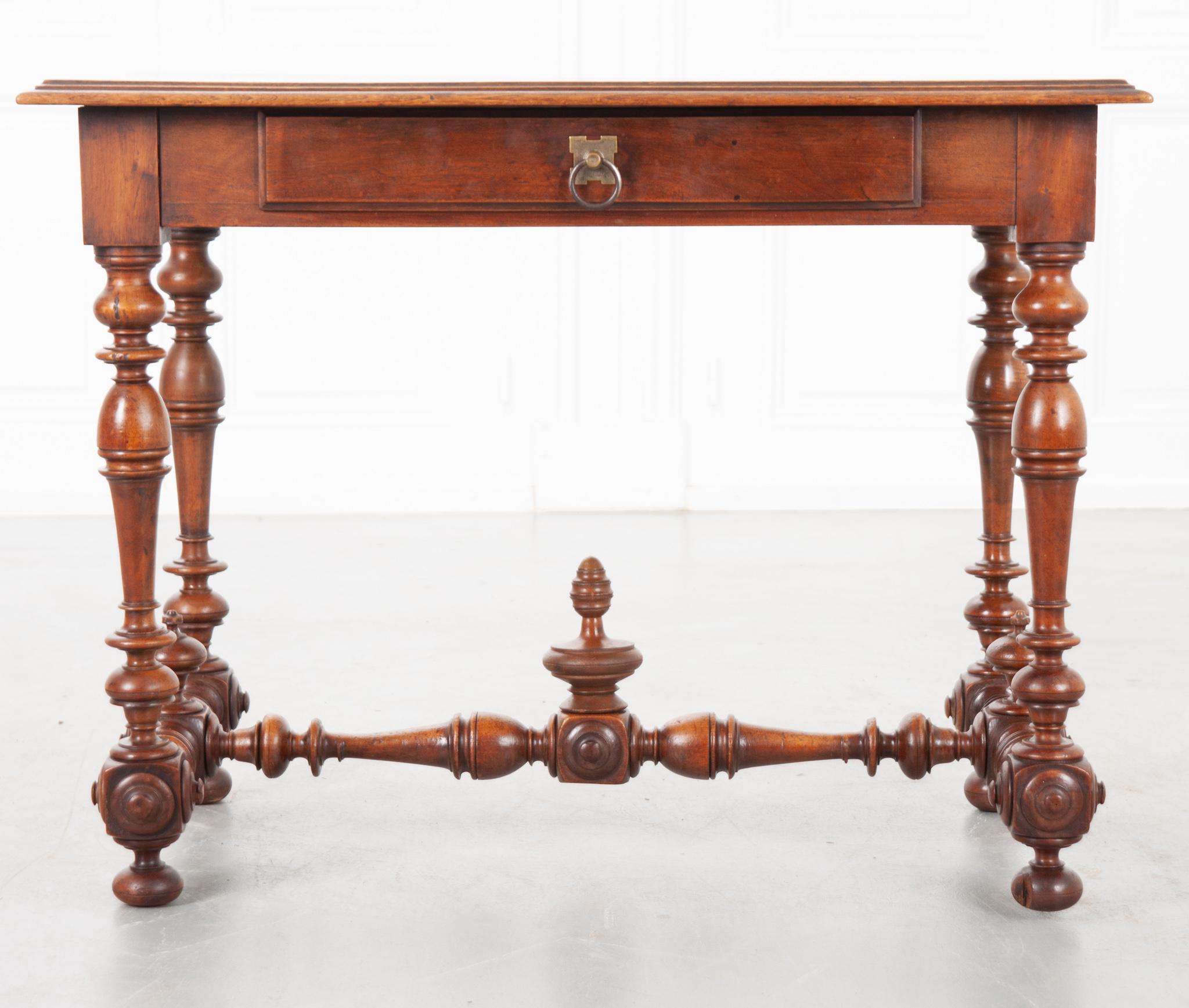 This is a good looking French 19th century oak and walnut writing table. The table’s apron has a single drawer opened by a worn brass pull. It has four turned legs and stretchers across the center and sides with three finials across them. Our table