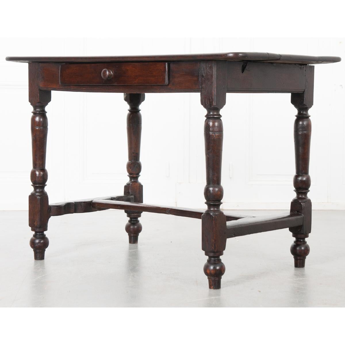 This is a French 19th century oak center table. The desk is put together with wood pegs. There are three wide boards across the top that rest on the apron, which has a single drawer with a wood knob. Turned legs support this piece and are connected