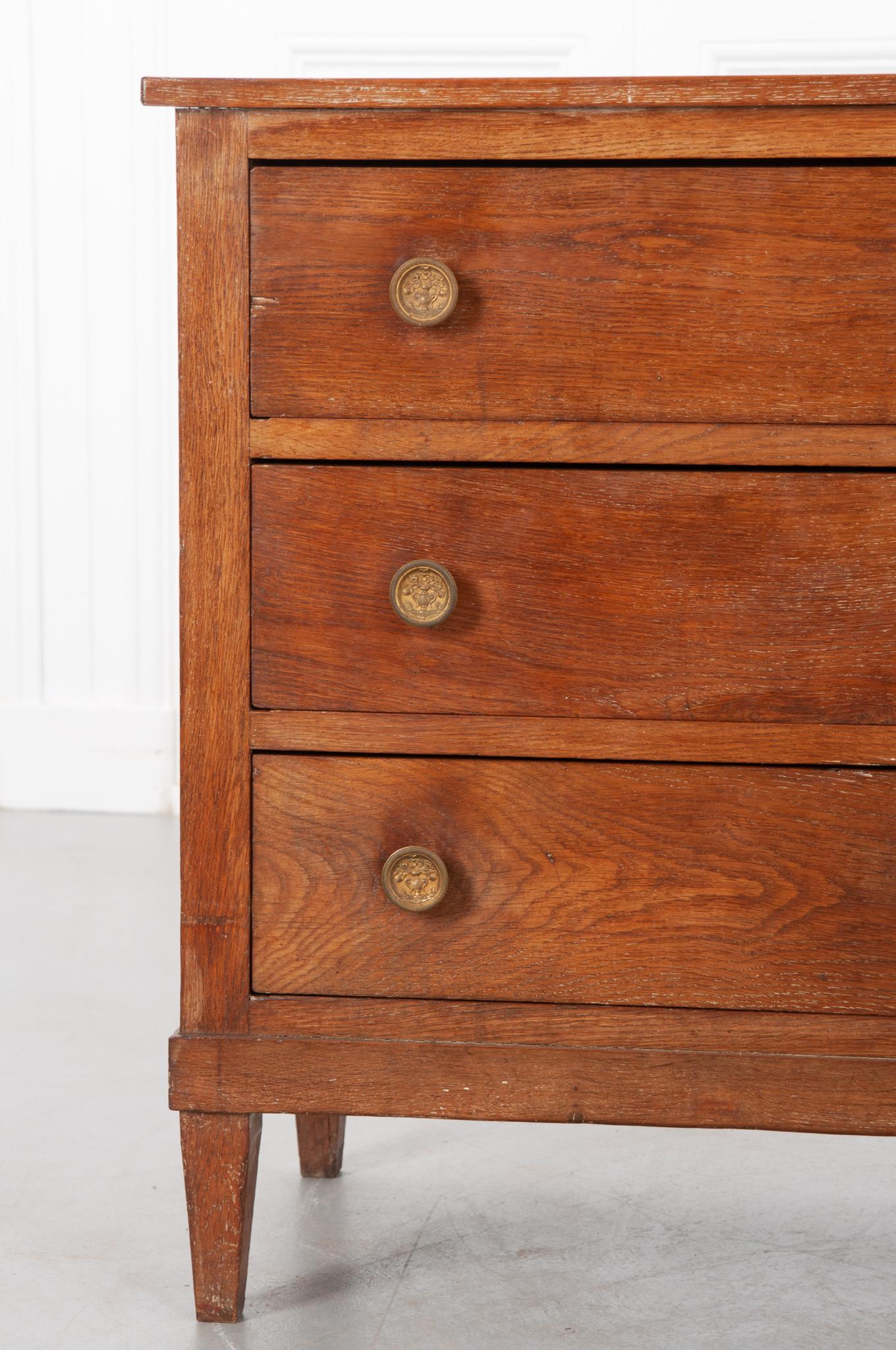A handsome three drawer commode stripped of paint and polished. It has beautiful oak tones. The lines are simple, but it is dressed up by the lovely details of the brass knobs – a vase of flowers. The drawers have no keys. They do have matching