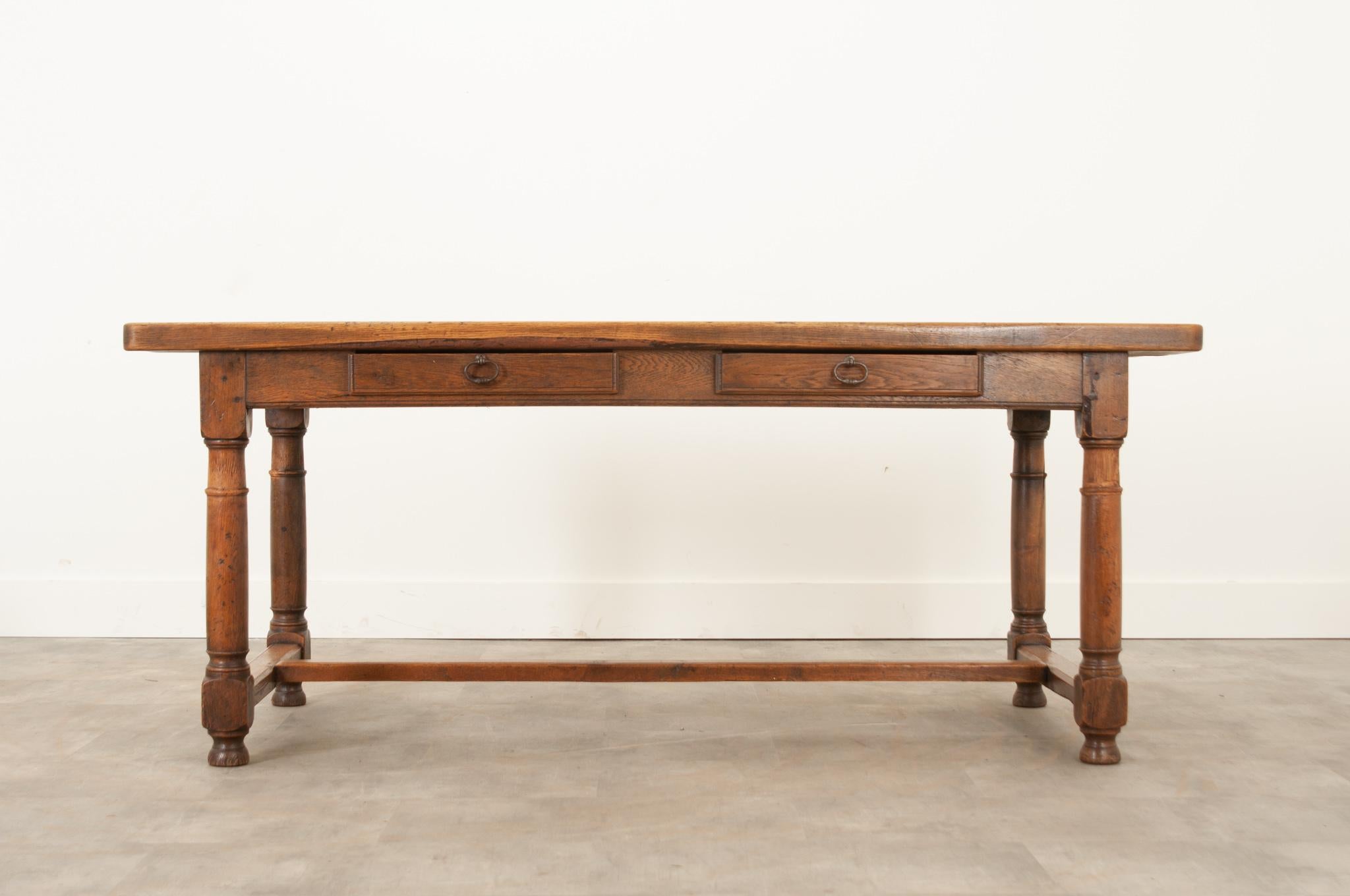 This rustic farm table was handcrafted in 19th century France from solid oak and built to stand the test of time. The thick top showcases the trademark knots in the woodgrain and a fantastic patina. The around houses two narrow drawers fixed with