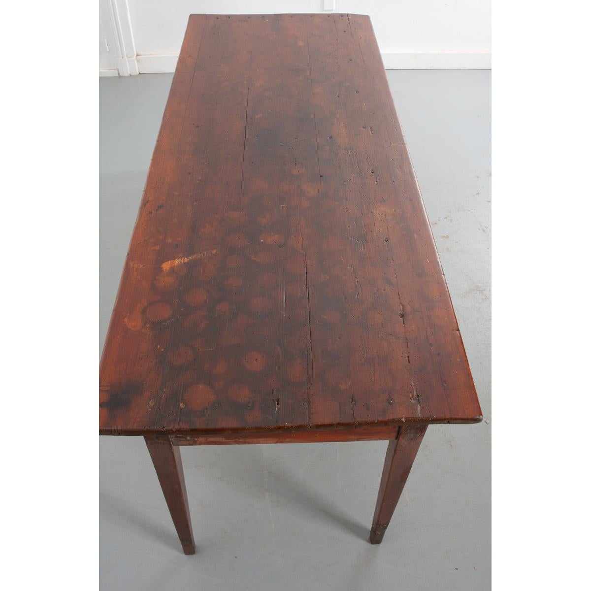 This charming 19th century French farm table has a wonderful patina. The sturdy pine top bears the marks of many lives that only add to the antique quality of the table. Measuring over 6 feet long, approximately 10-12 places can be set depending on