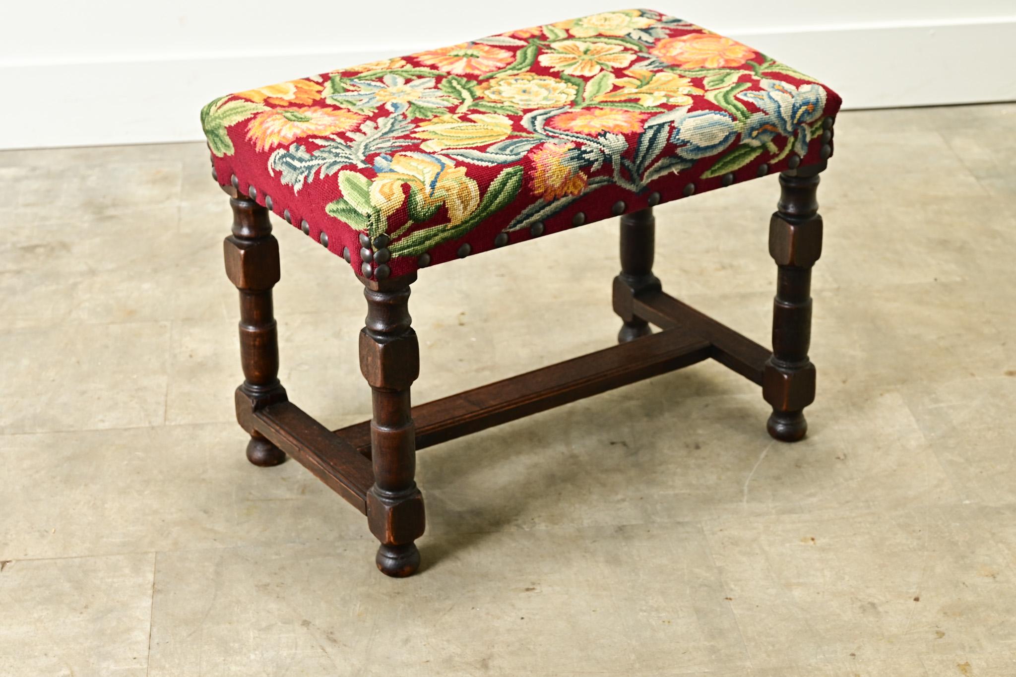 A French oak and tapestry stool made in the 1800’s. This comfortable stool is upholstered in a bright and colorful floral needlepoint tapestry with nailhead trim. Raised on turned solid oak legs connected to a H-shaped stretched for additional