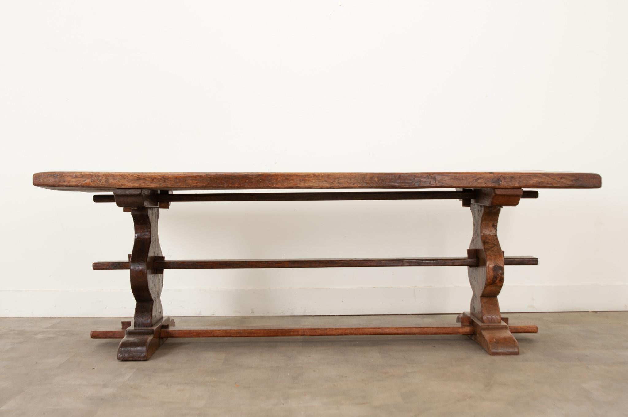 A handsome French trestle base table is made using hand cut solid oak boards. The two inch thick top sits over a pair of hourglass shaped pedestals connecting with three stretchers. This table has been recently polished with a French paste wax and