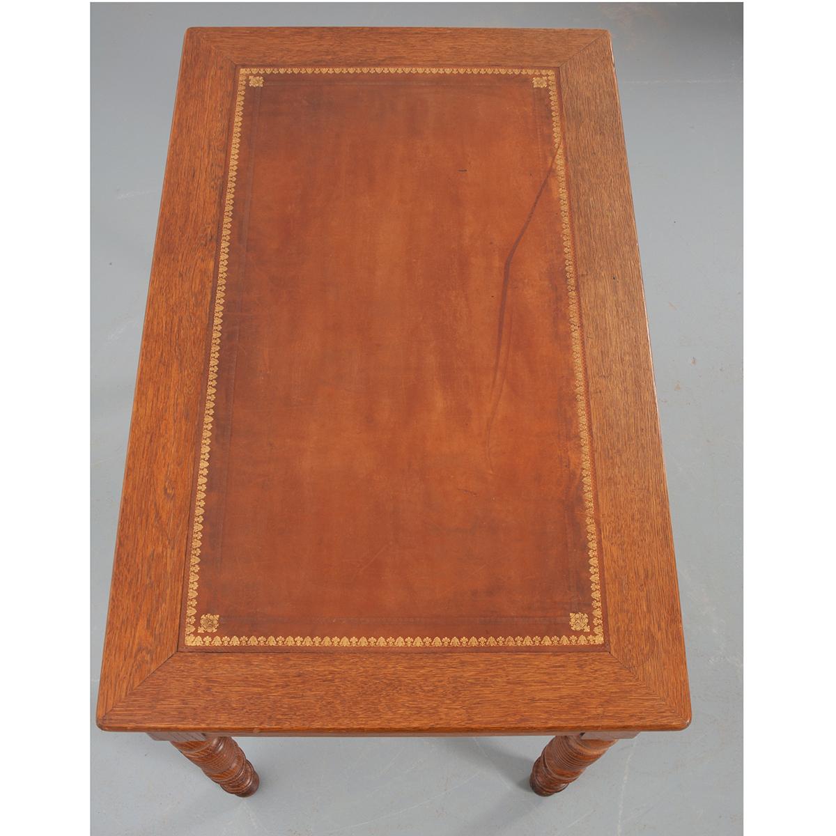 An extraordinary oak desk could serve as an occasional table or a small writing desk. The writing surface has a beautiful inset, warm cognac color leather top with gold filigree banding and two different tooled designs. Two locking drawers are