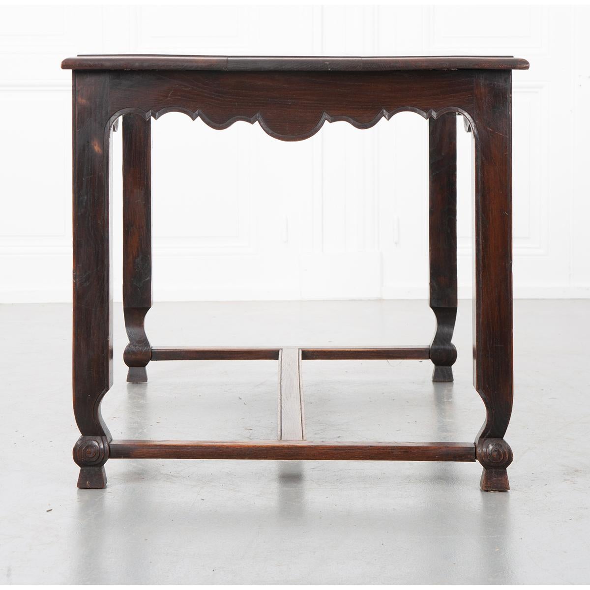 This unique oak writing desk, c. 1890, is simply gorgeous. The three plank top has rick, deep graining and a wonderfully aged patina. It sits above a scalloped apron on all four sides. The apron has a beveled-like trim carved on its edge, extending