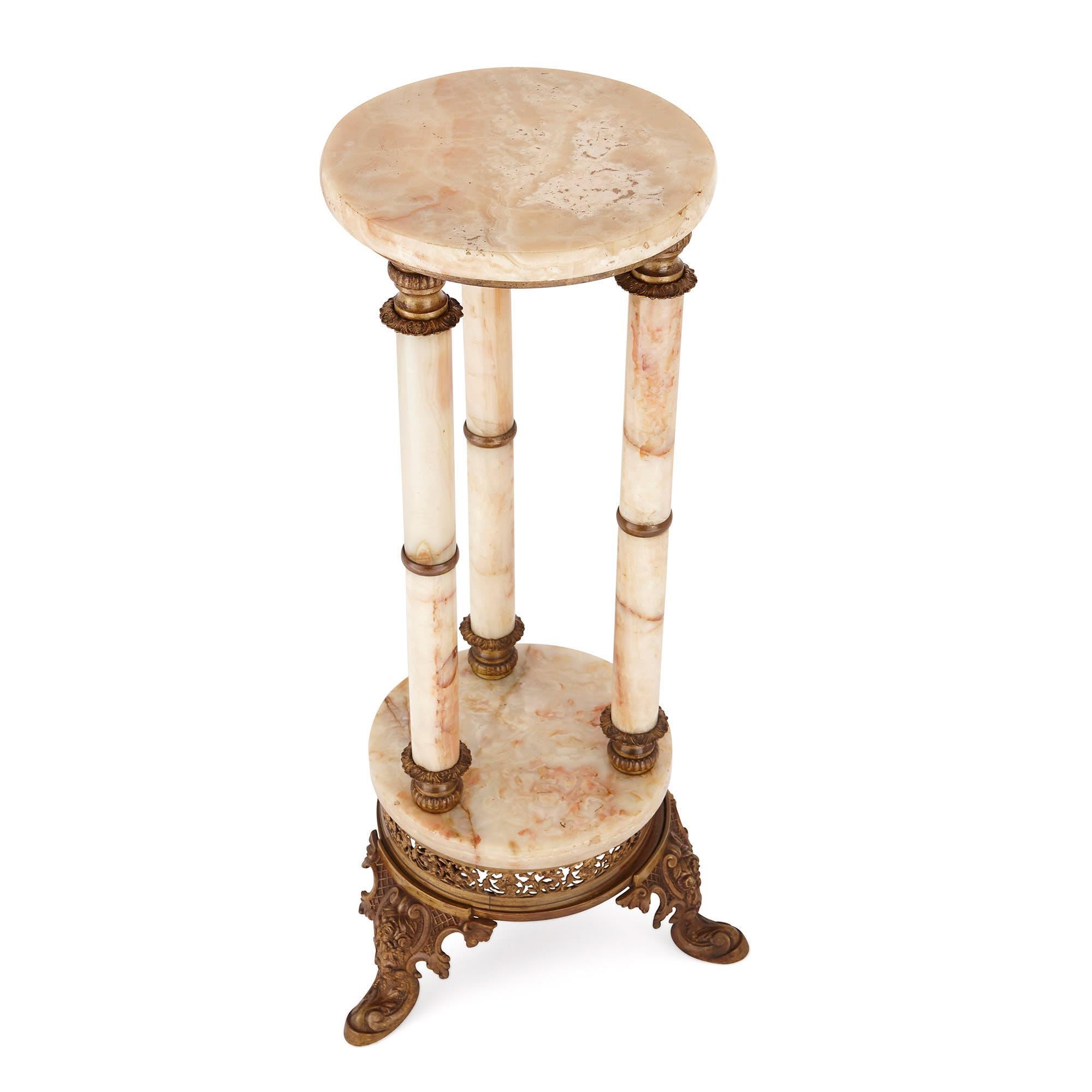 This cream-colored onyx and gilt metal Stand was crafted in France in the late 19th century. The piece features a circular onyx top, with a gilt metal base, which is supported on three columns. These columns have fluted and frilled gilt metal