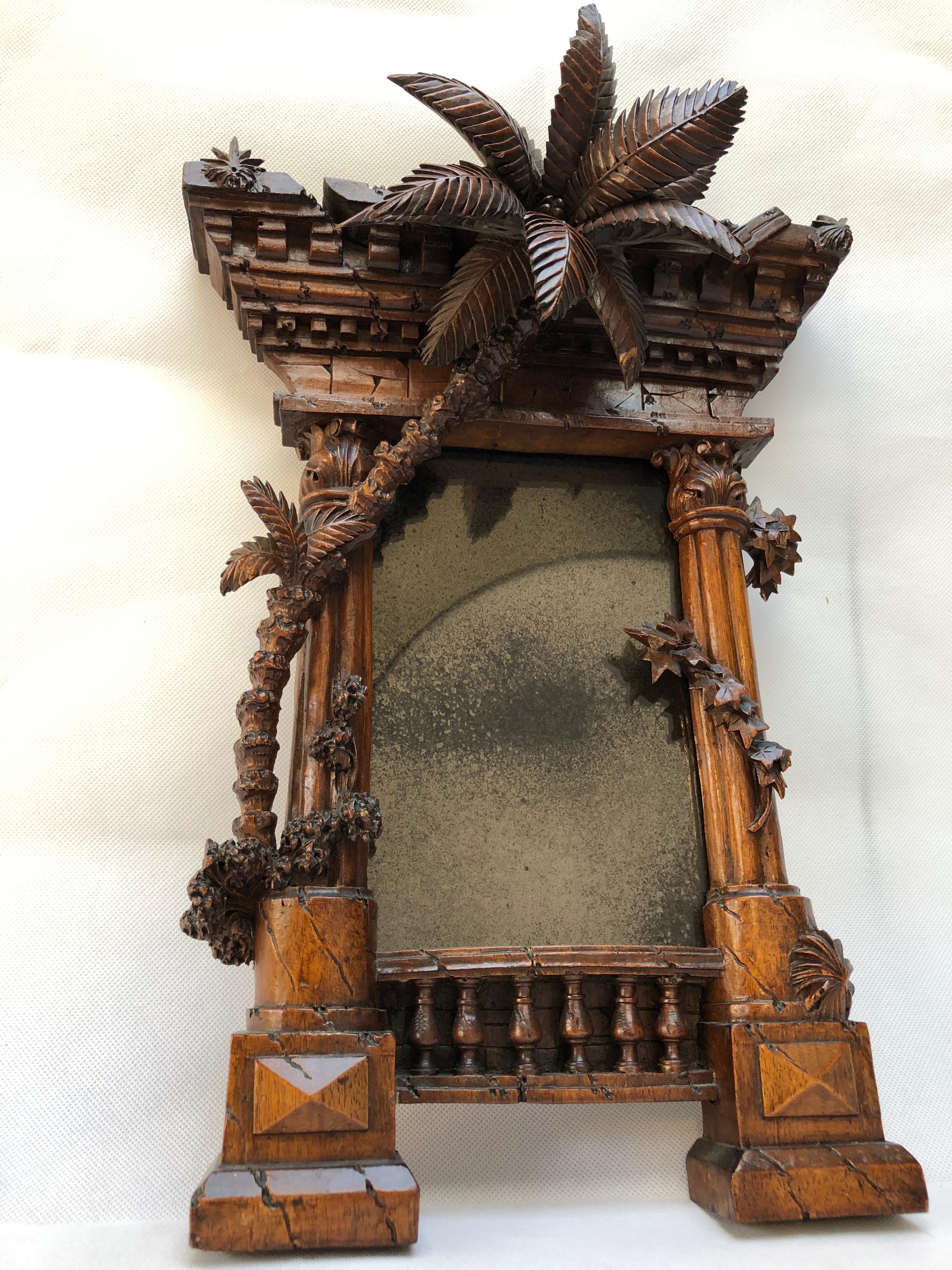 A French 19th century Orientalist carved walnut frame modelled as a Classical ruin
The rectangular mirror plate surmounted by an architectural capital flanked to each side by a fluted column with foliage and a large palm tree, the base with a