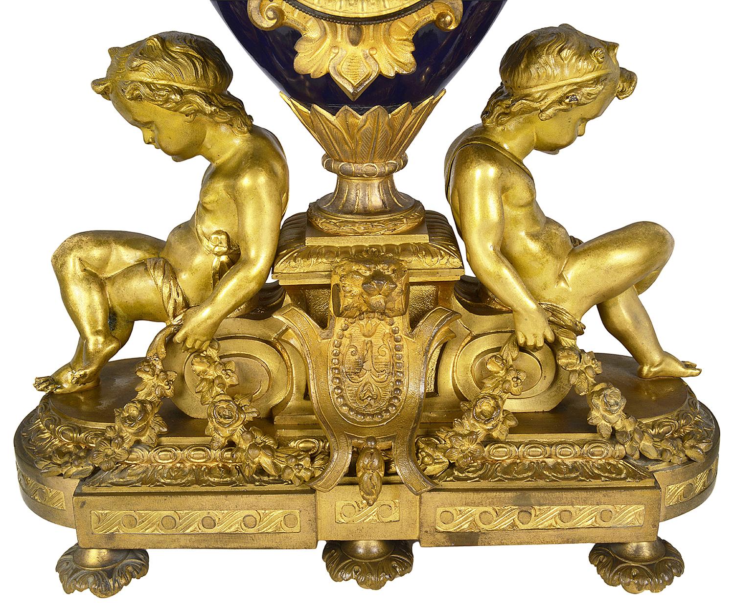 A very impressive late 19th century French gilded ormolu and cobalt blue porcelain urn clock set, the clock having seated putti holding garlands of flowers, the clock movement having an eight day duration that strikes on the hour and half hour. Lion