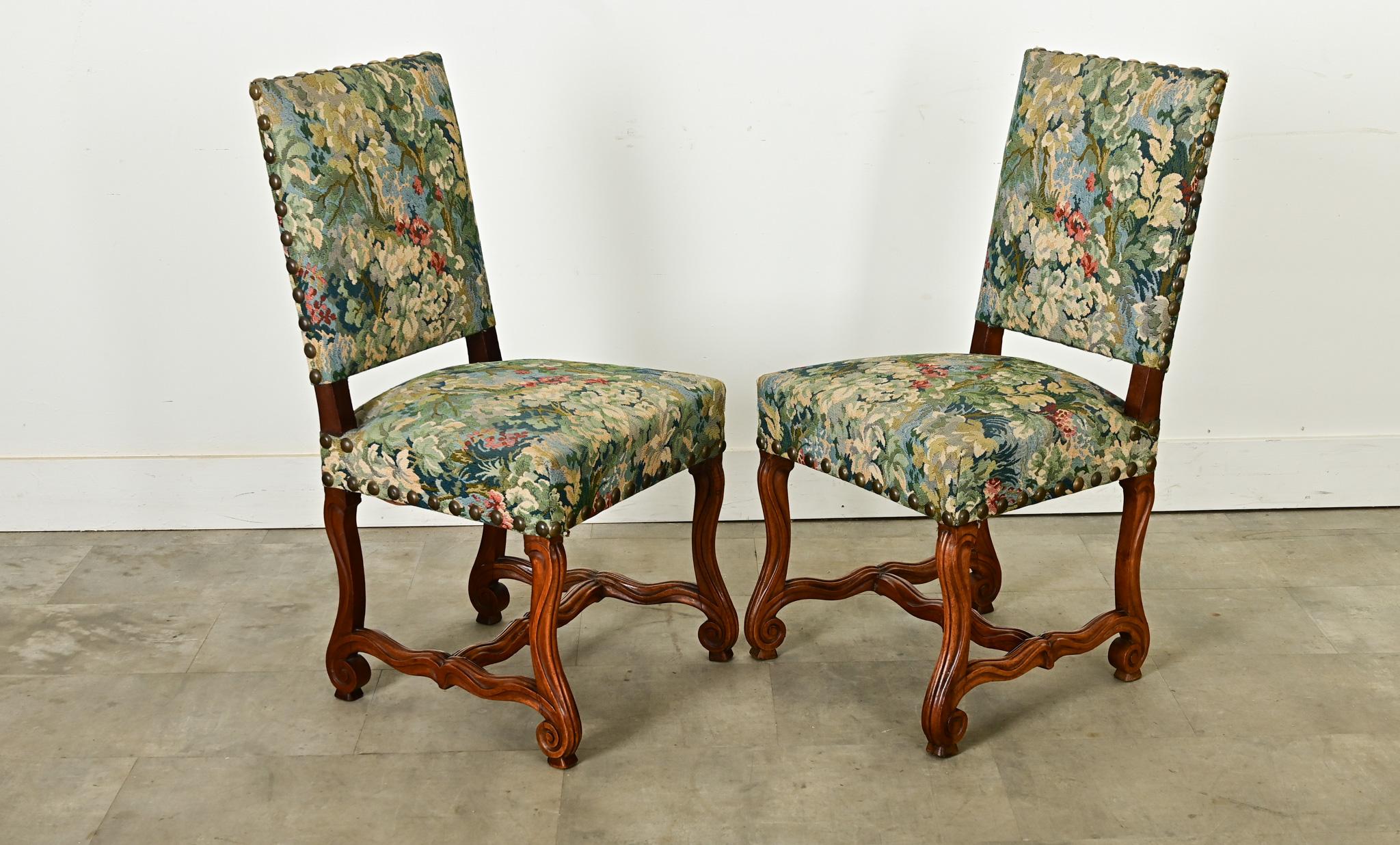 Coppia di poltroncine in noce intagliato Os de Mouton del XIX secolo con tappezzeria colorata ad ago sostenuta da grandi borchie in ottone. La stoffa tessuta a mano raffigura immagini lussureggianti di un fitto fogliame nei toni del blu, del verde e